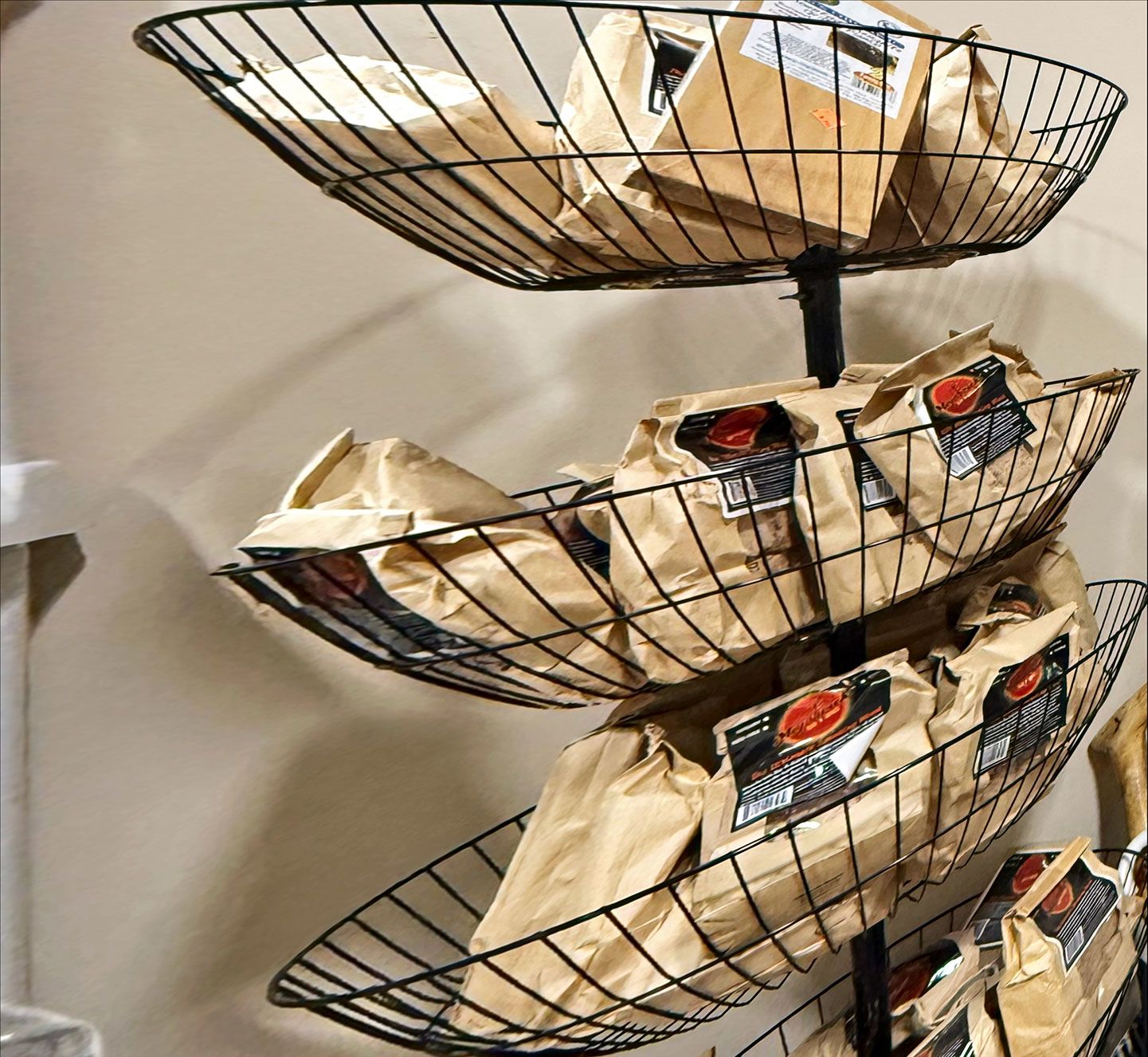 Three-tiered wire display holding brown paper bags of product, mounted on a wall.