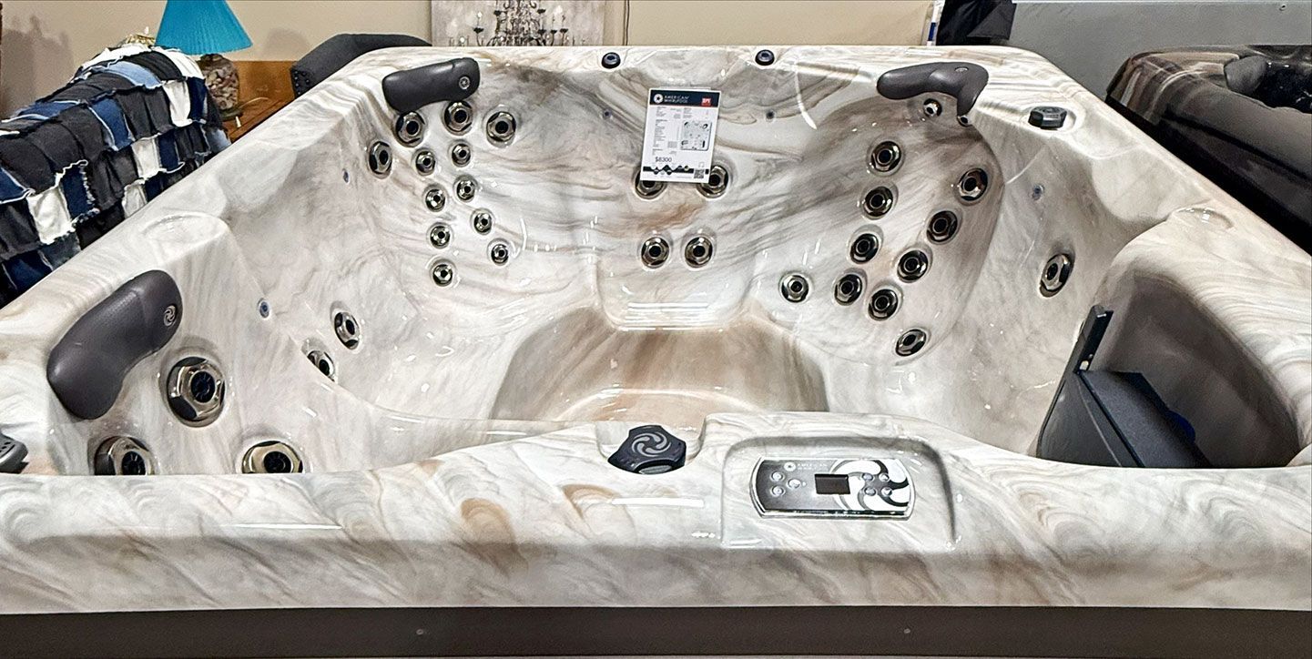 A large hot tub with multiple jets is displayed indoors. It has a light marbled appearance.