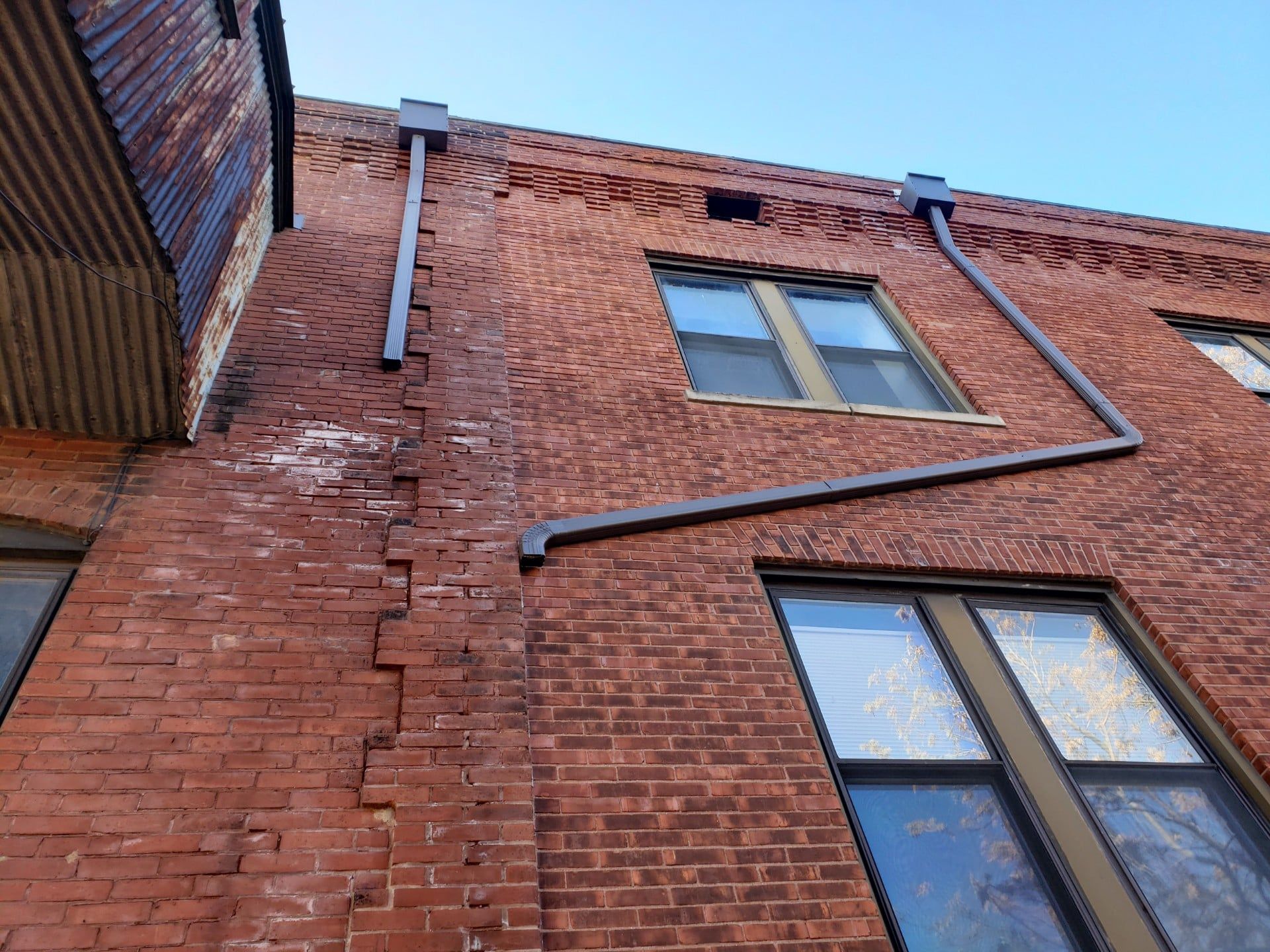 Red brick building with cracks and a metal gutter.