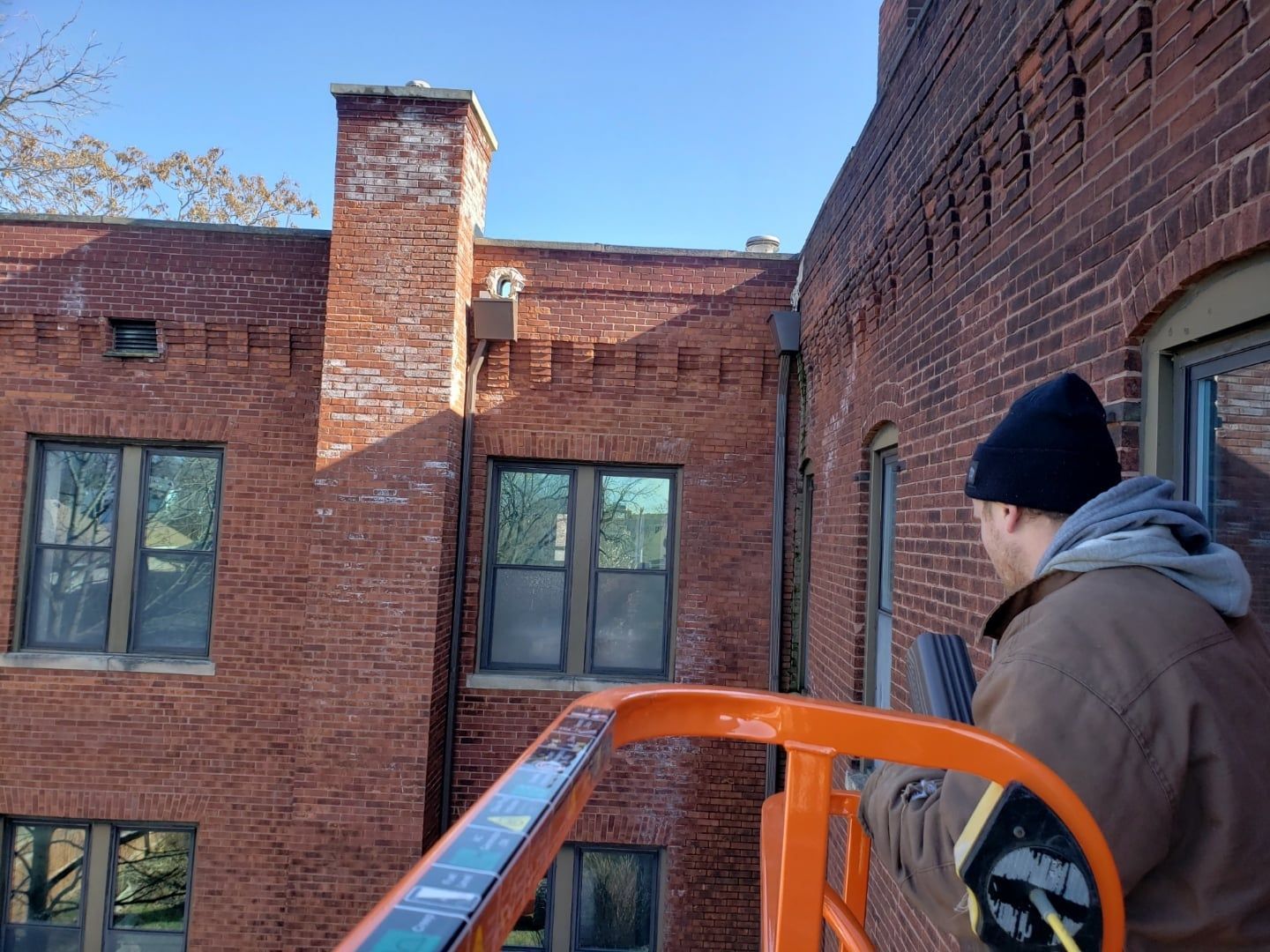 Brick building exterior with a person in a lift, looking at the wall.