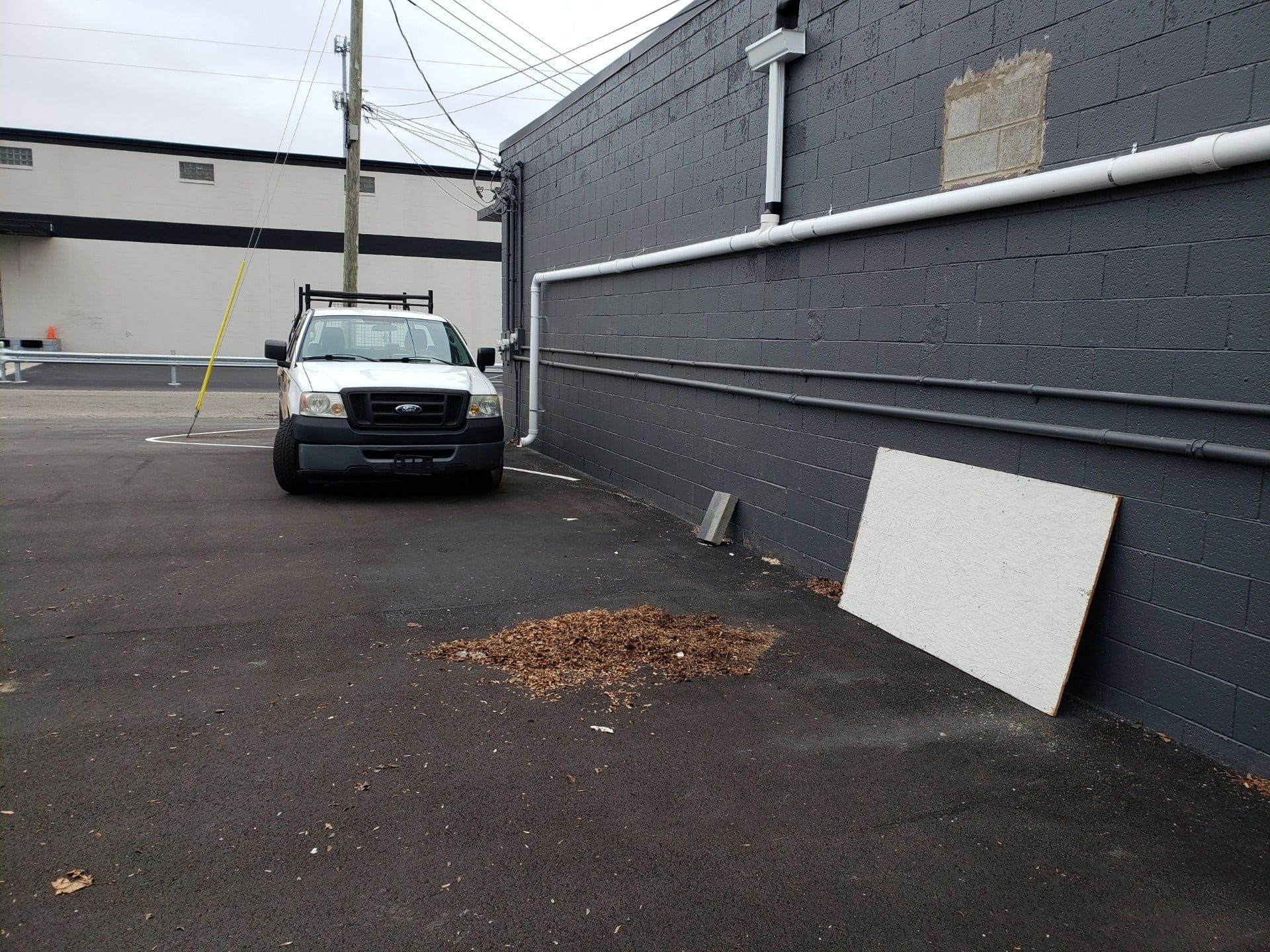 A white work truck parked in an asphalt lot next to a dark gray brick wall.