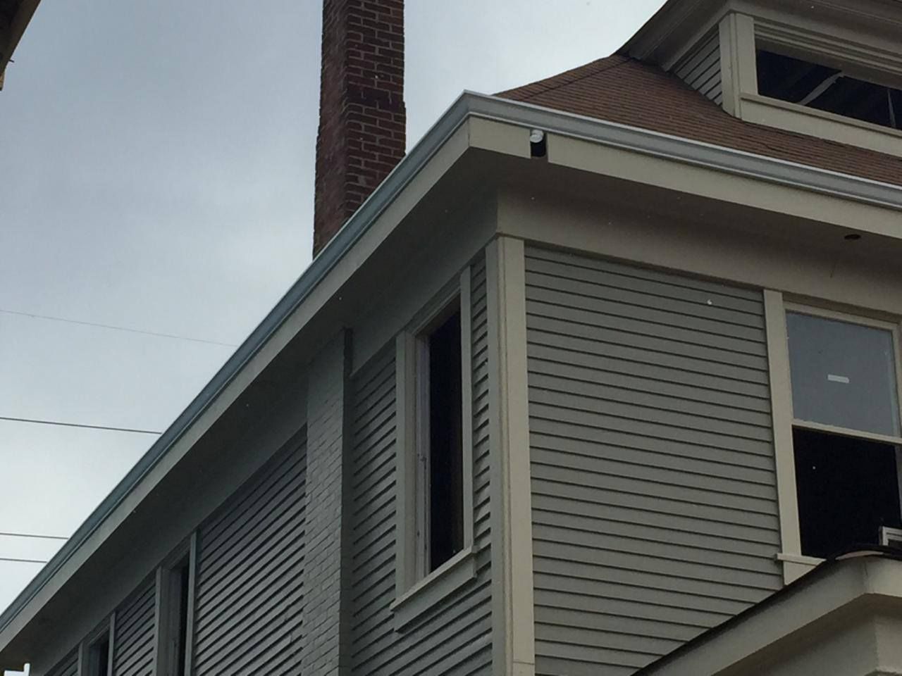 Exterior corner of a two-story house with gray siding, white trim, and a brick chimney.