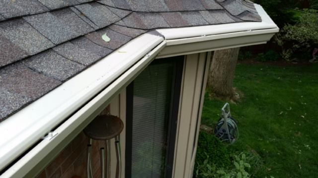 White gutters along roof edge, brown shingles, beige window frame, green grass.