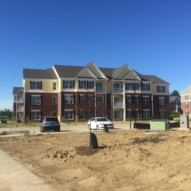 Apartment building with brick facade and balconies; two cars parked in front, clear blue sky.