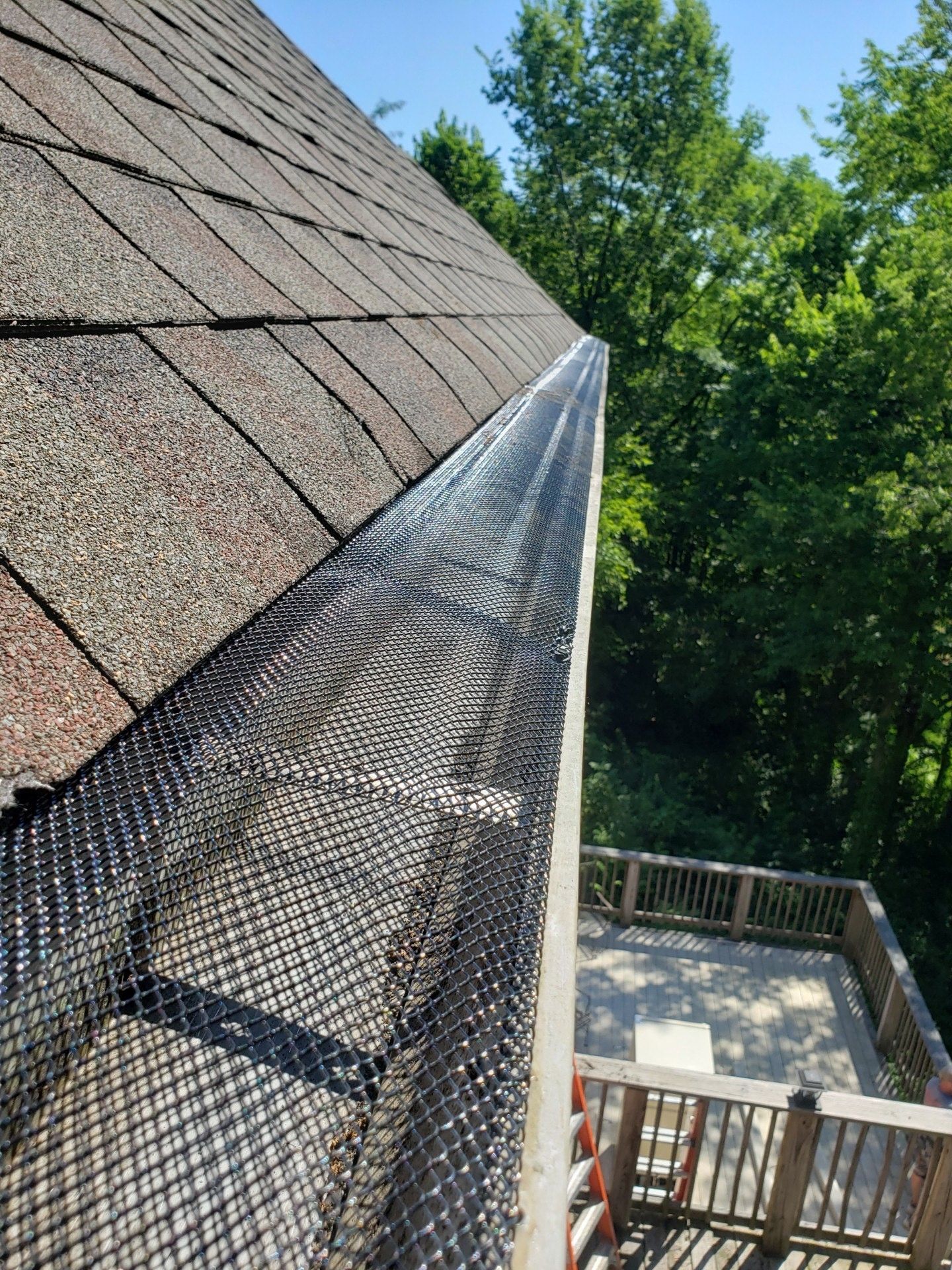 Gutter with mesh guard on a roof, with a deck visible in the background against a blue sky.