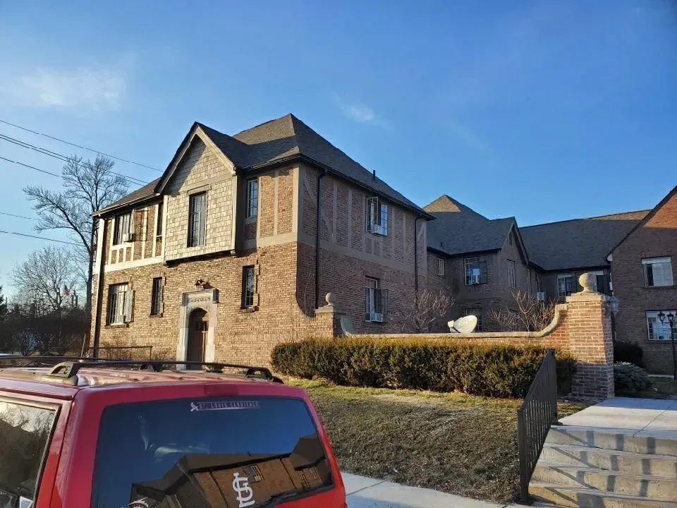 Brick building with dark roof, red car parked in front, clear blue sky.