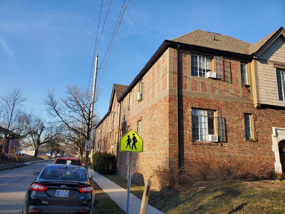 Apartment building with brick exterior, sidewalk, street, car, and a school zone sign on a sunny day.