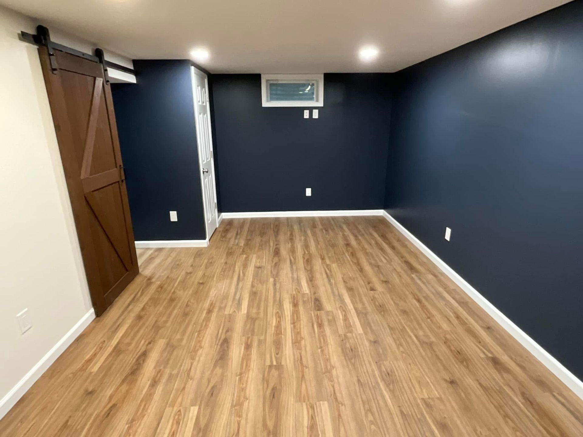 Empty room with blue walls, wood floor, barn door, and a small window air conditioner.