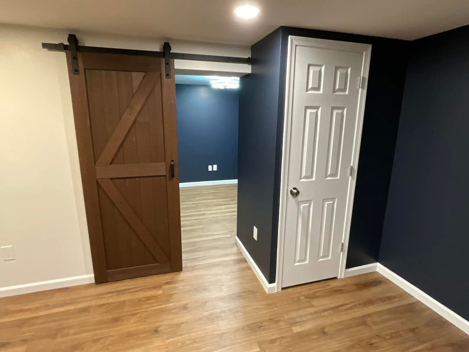 Empty room with wood floor, dark blue walls, a barn-style sliding door, and a white door.