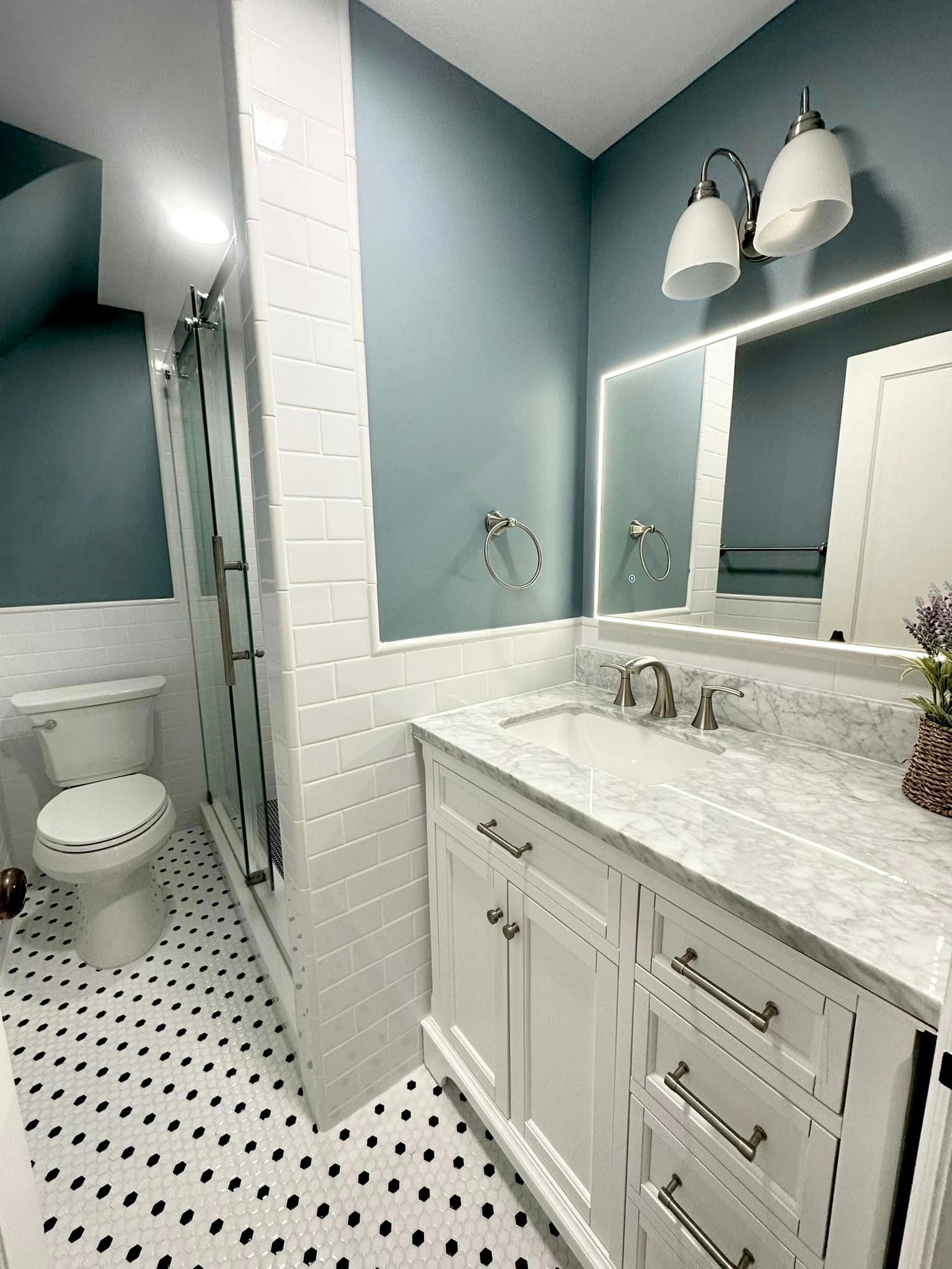 Small bathroom with white vanity, black-and-white floor tiles, mirror, and light blue walls.