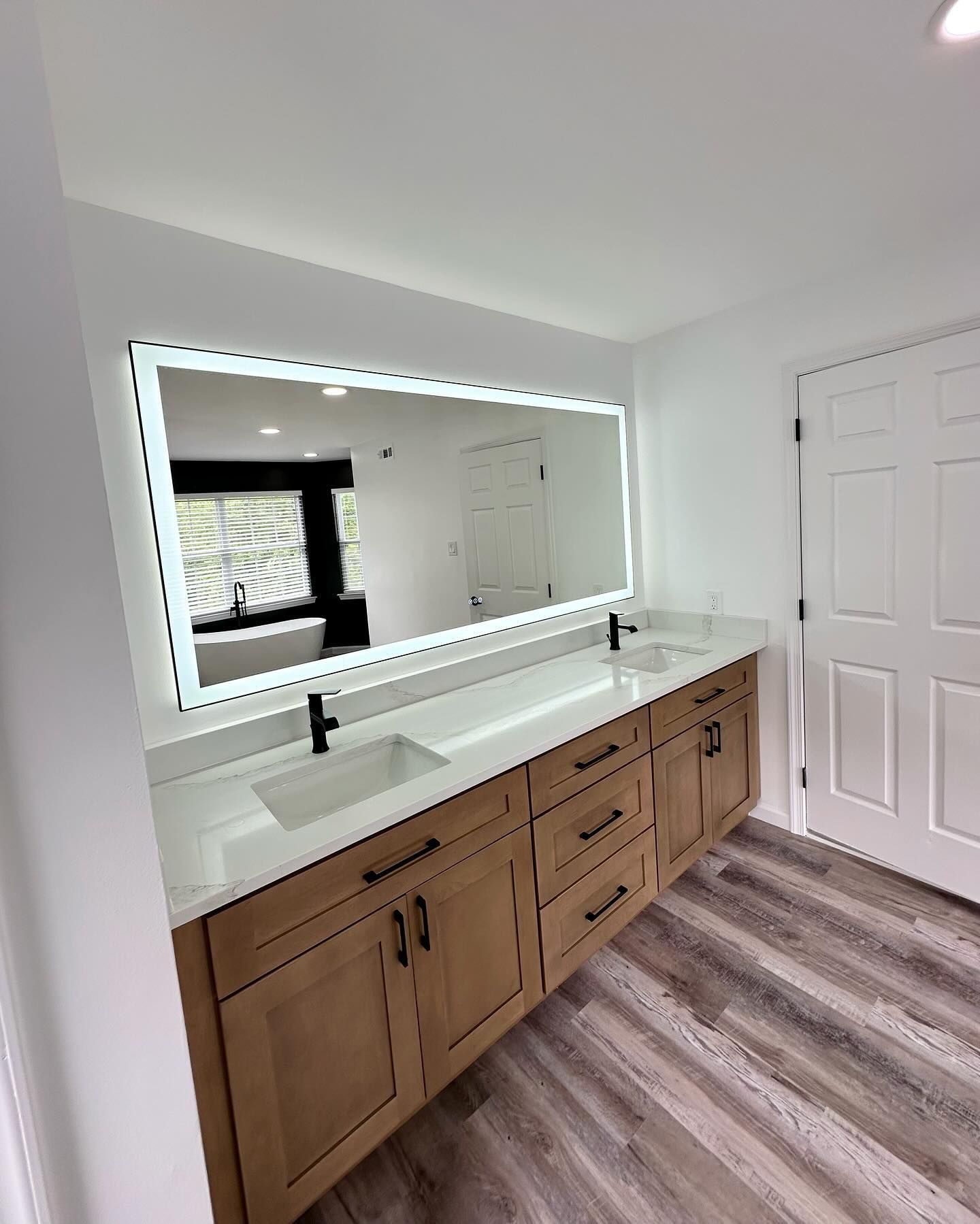 Modern bathroom vanity with long mirror, double sinks, wood cabinets, and gray flooring