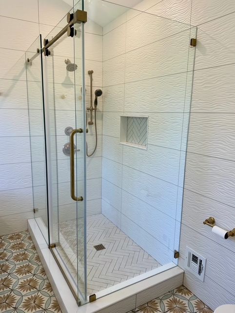 Glass-enclosed tiled shower with bench, chrome grab bars, and built-in shelf niche.