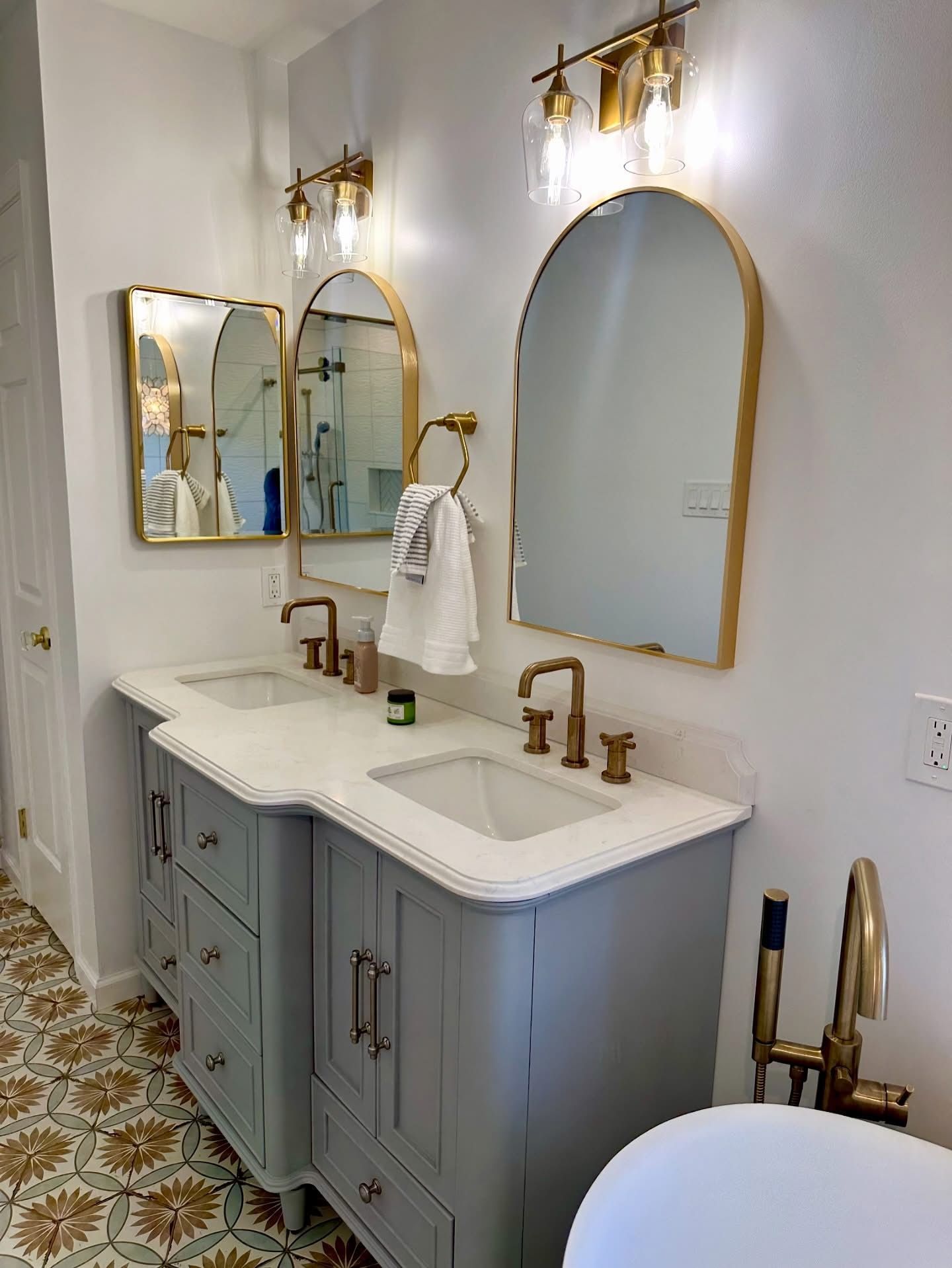 Elegant white bathroom with gold accents, twin mirrors, and a patterned tile floor.