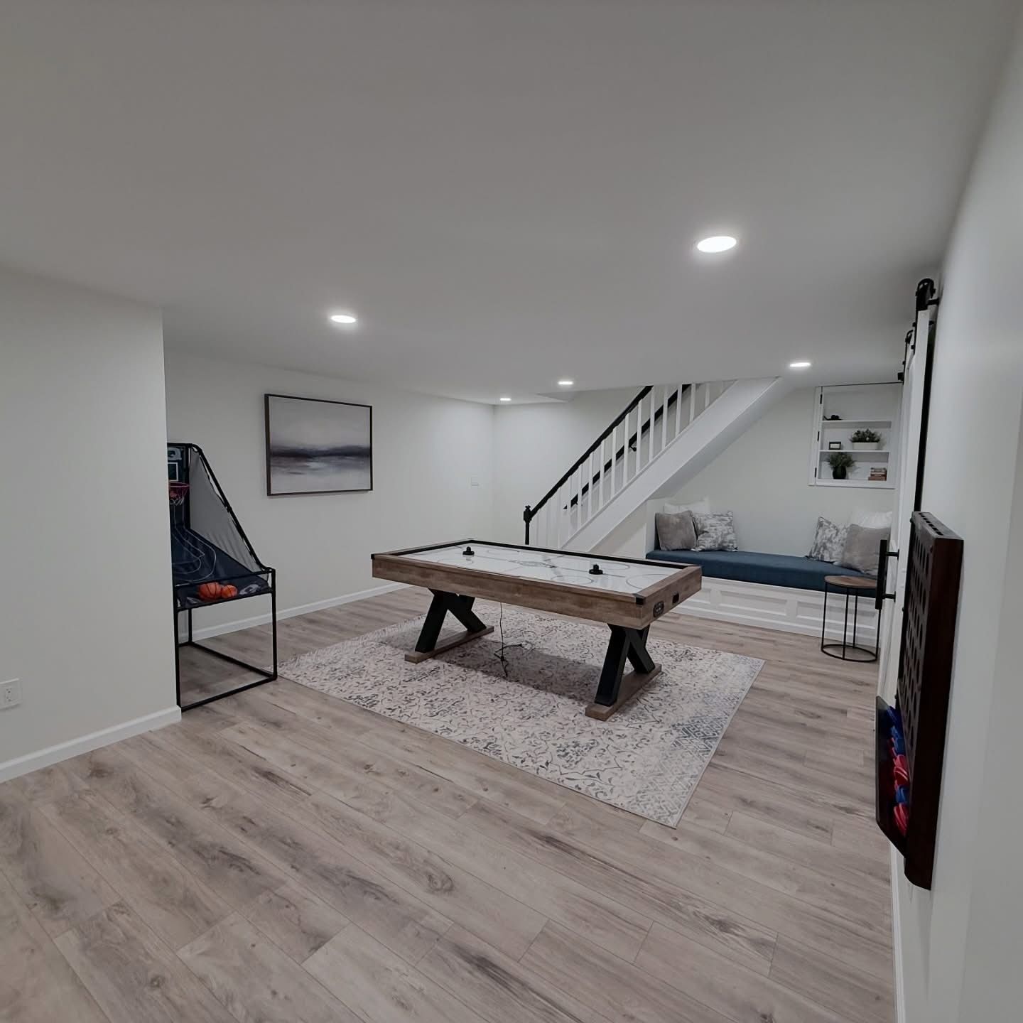 Modern basement rec room with pool table, foosball, ping-pong table, and staircase under recessed lights