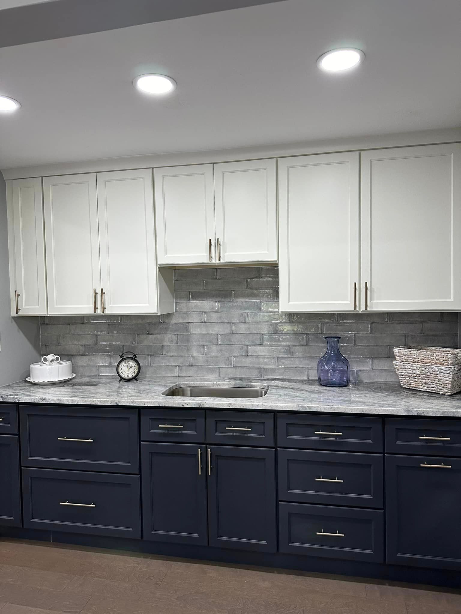 Modern kitchen with white upper cabinets, navy lower cabinets, gray tile backsplash, and recessed ceiling lights