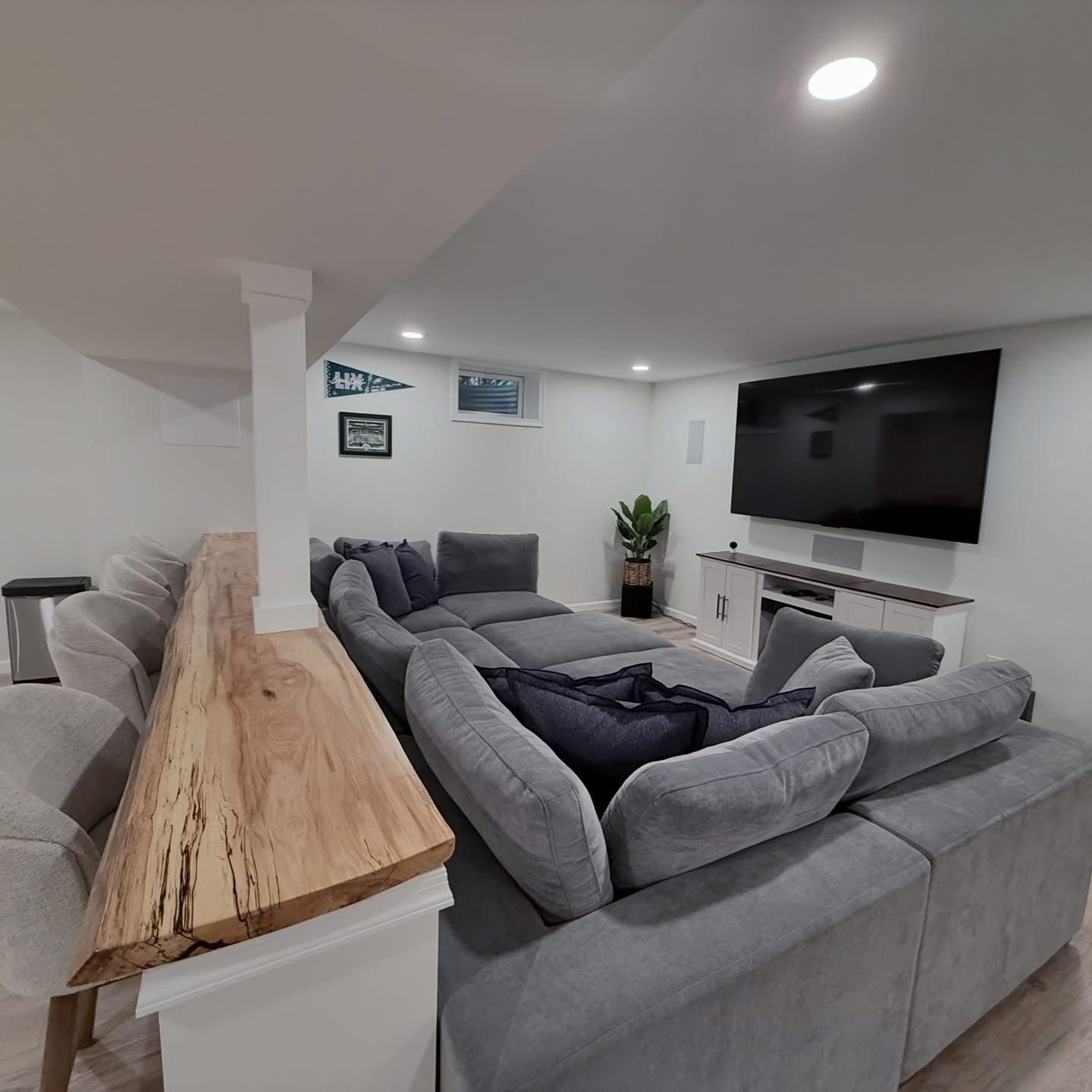 Modern living room with gray sectional sofa, large wall-mounted TV, and wood-topped railing.