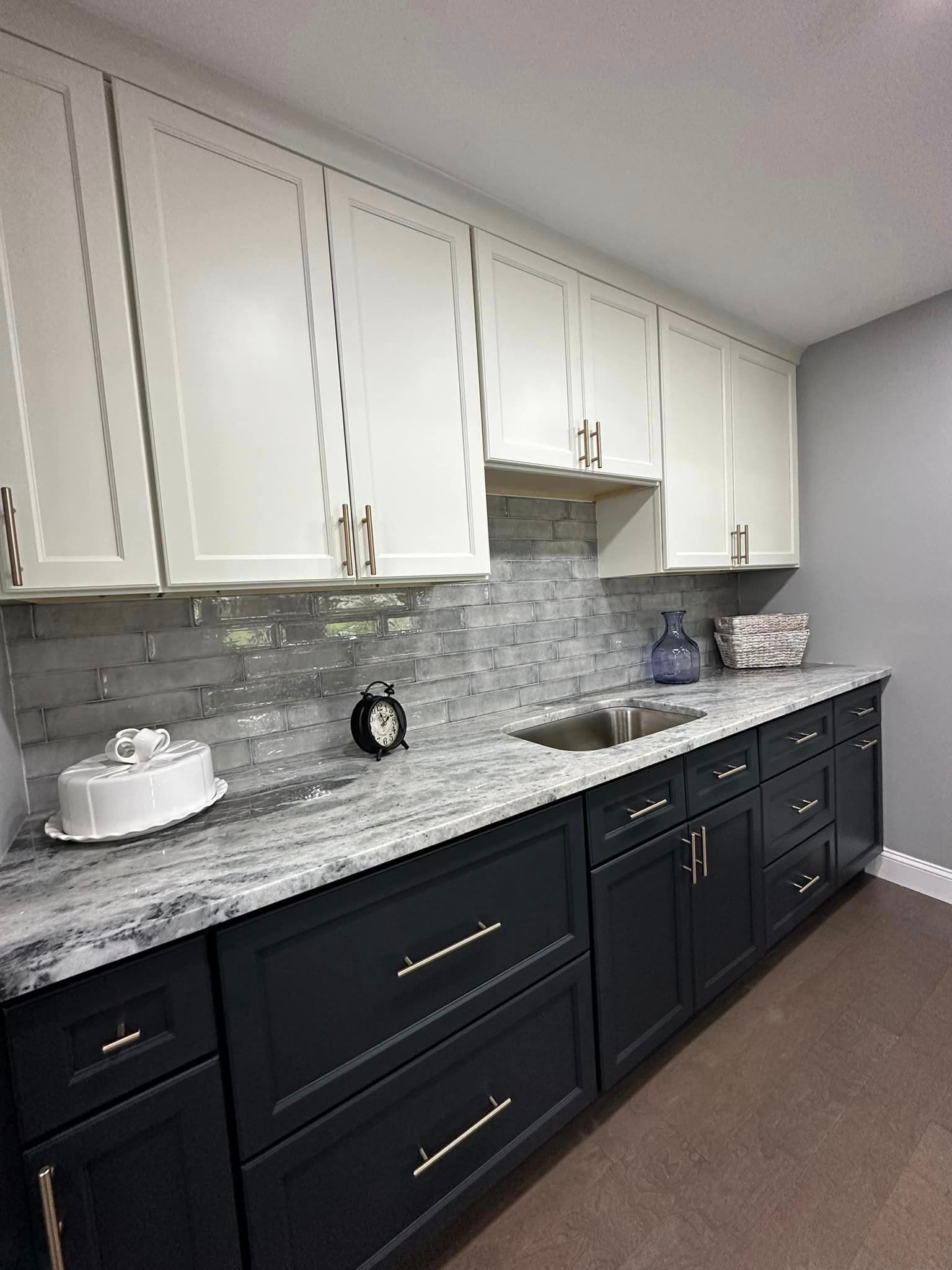 Modern kitchen with white upper cabinets, dark lower cabinets, gray backsplash, and granite countertop.