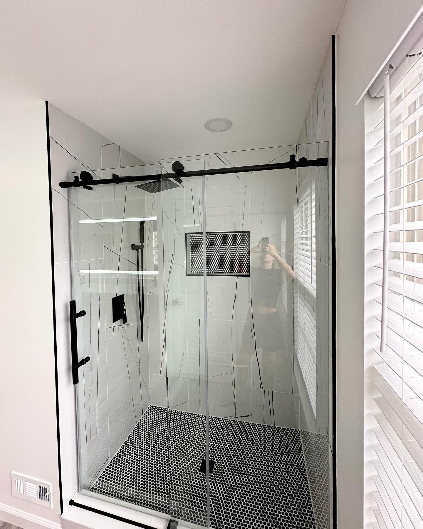 Modern bathroom with glass shower enclosure, black hardware, and patterned black-and-white floor tiles