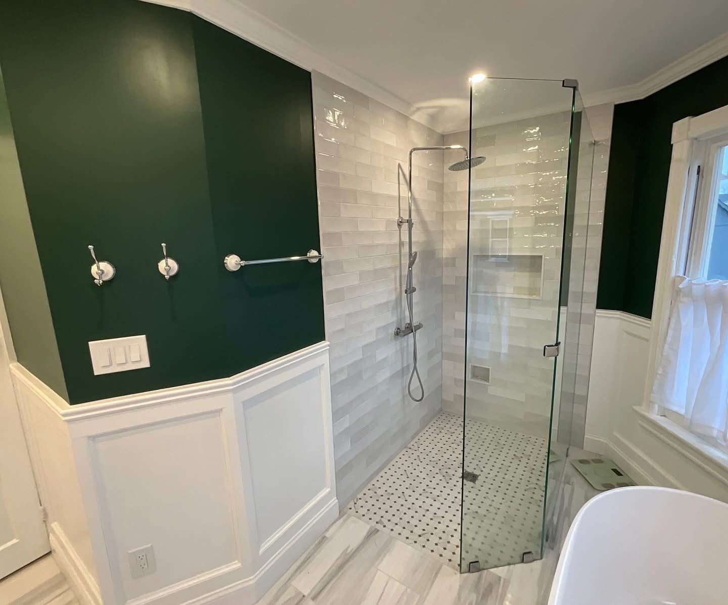 Bright bathroom with glass walk-in shower, green and white walls, and tiled floor.
