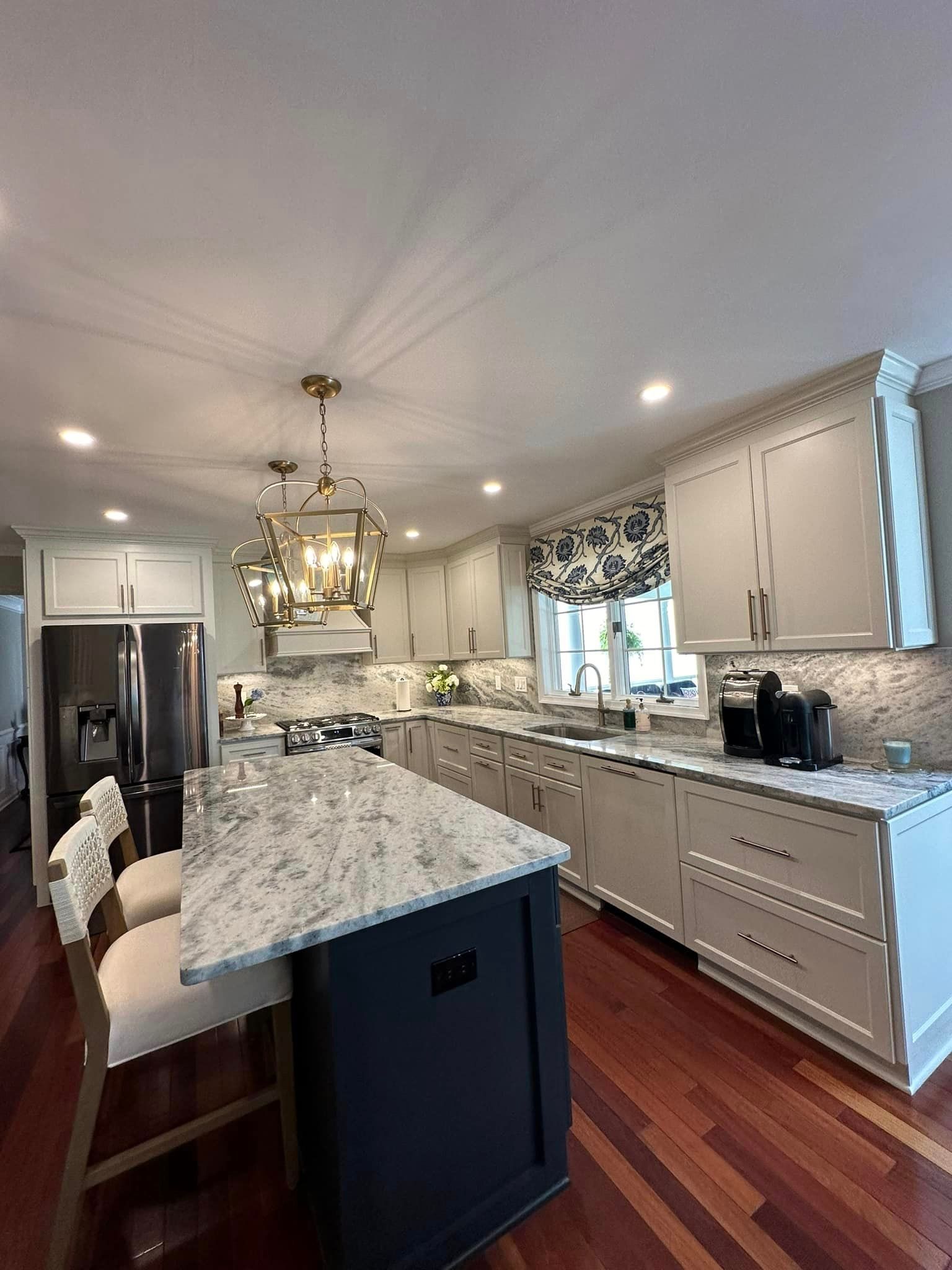 Bright kitchen with granite island, white cabinets, pendant light, hardwood floors, and stainless-steel fridge
