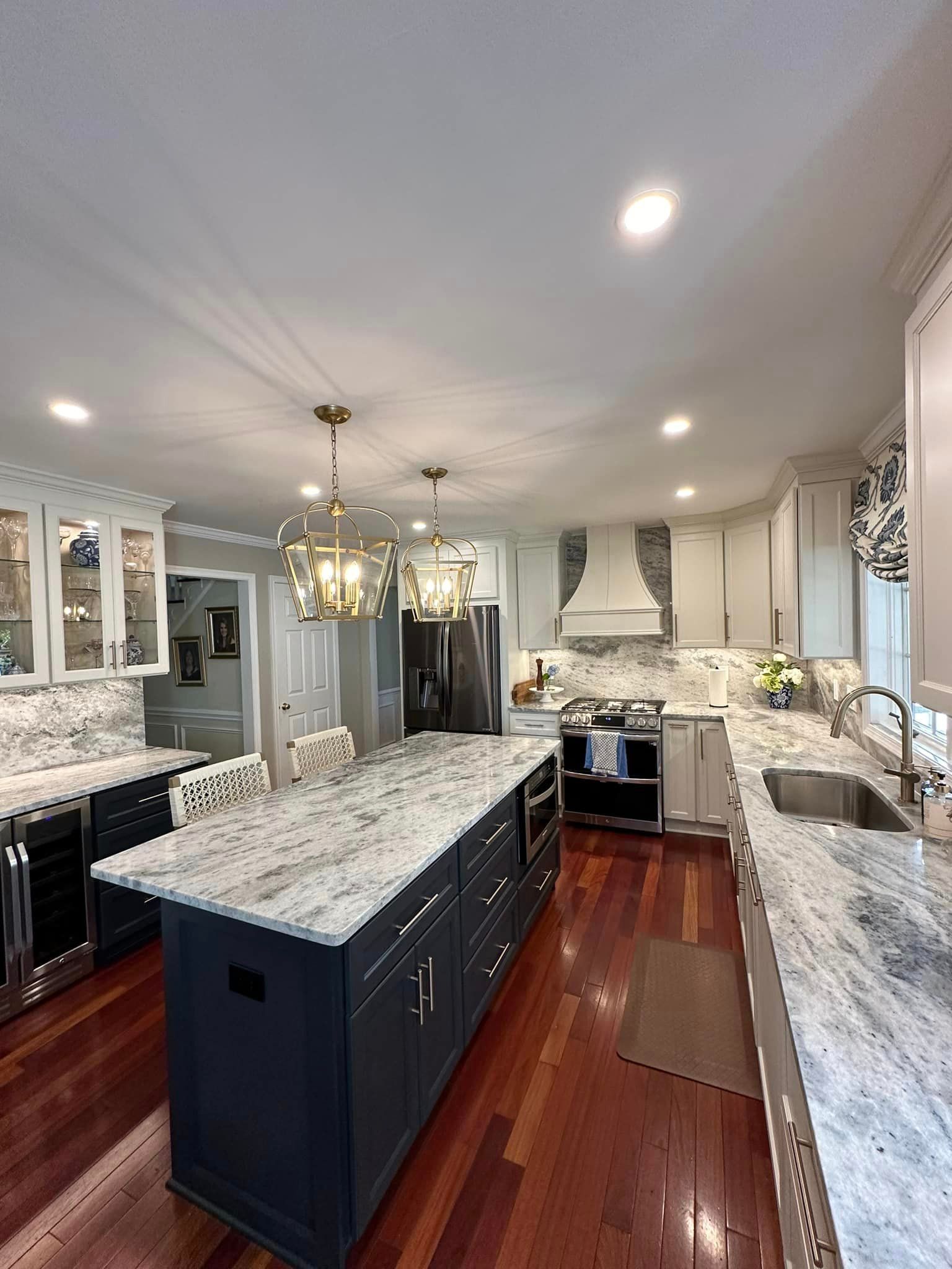 Bright kitchen with dark cabinets, marble island, hardwood floors, chandelier, and white appliances