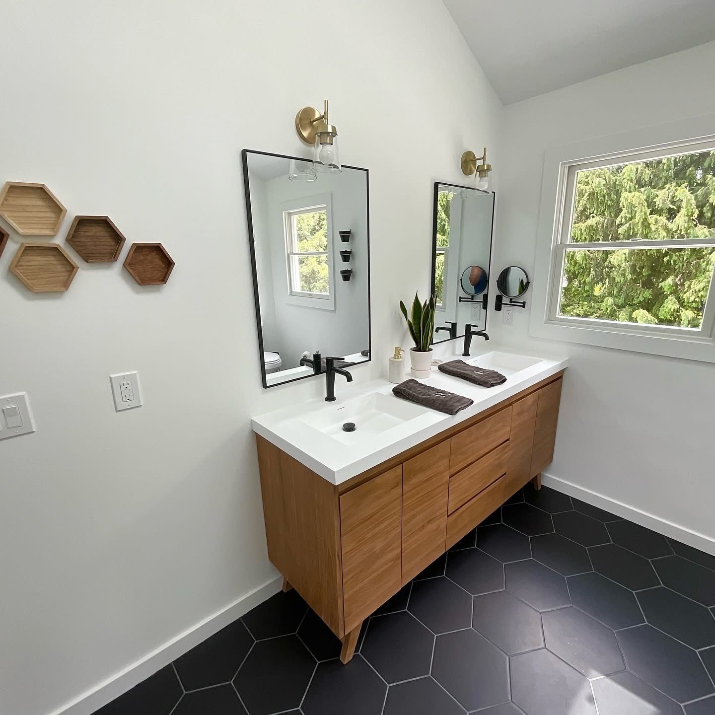 Modern bathroom vanity with twin mirrors, wood cabinets, black hex tile floor, and a window