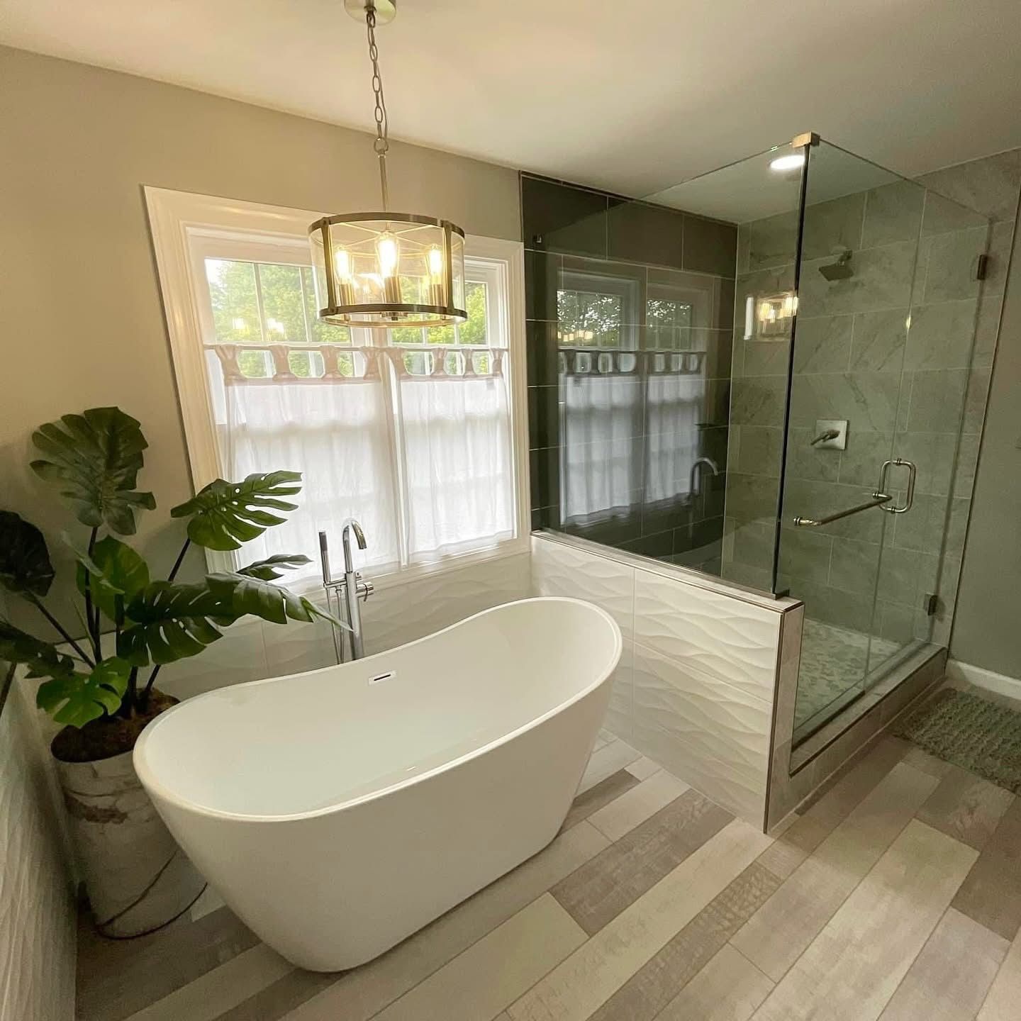 Modern bathroom with freestanding tub, glass shower, chandelier, and light wood flooring