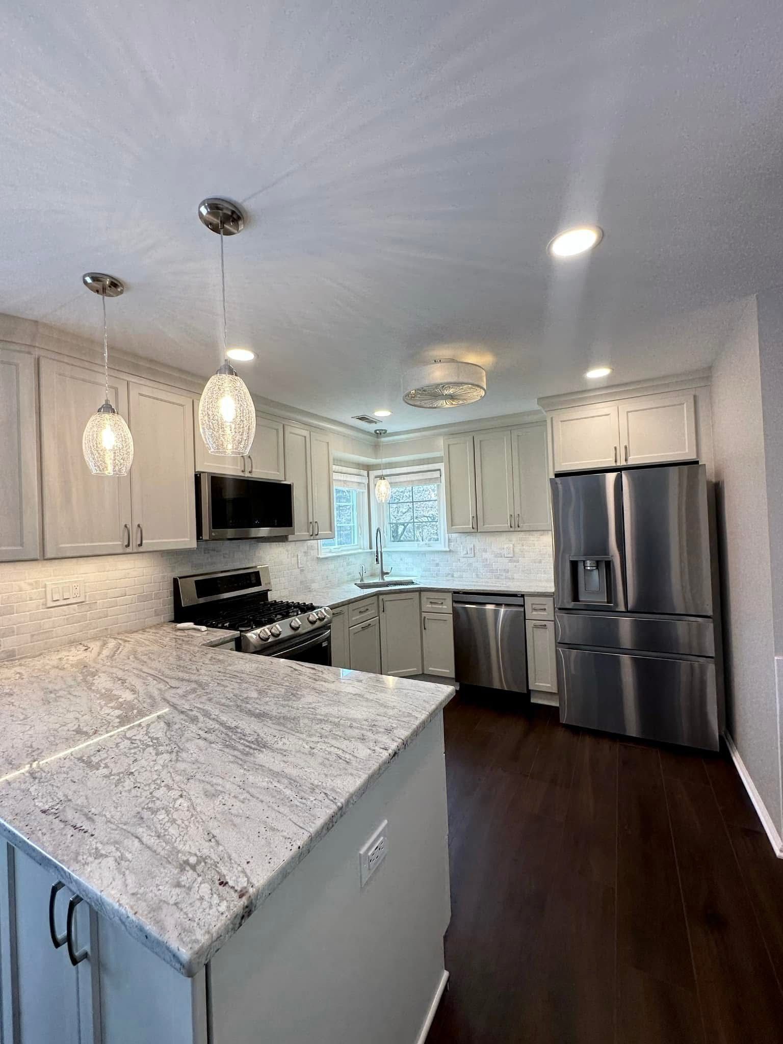 Modern white kitchen with granite island, stainless appliances, pendant lights, and dark wood floors