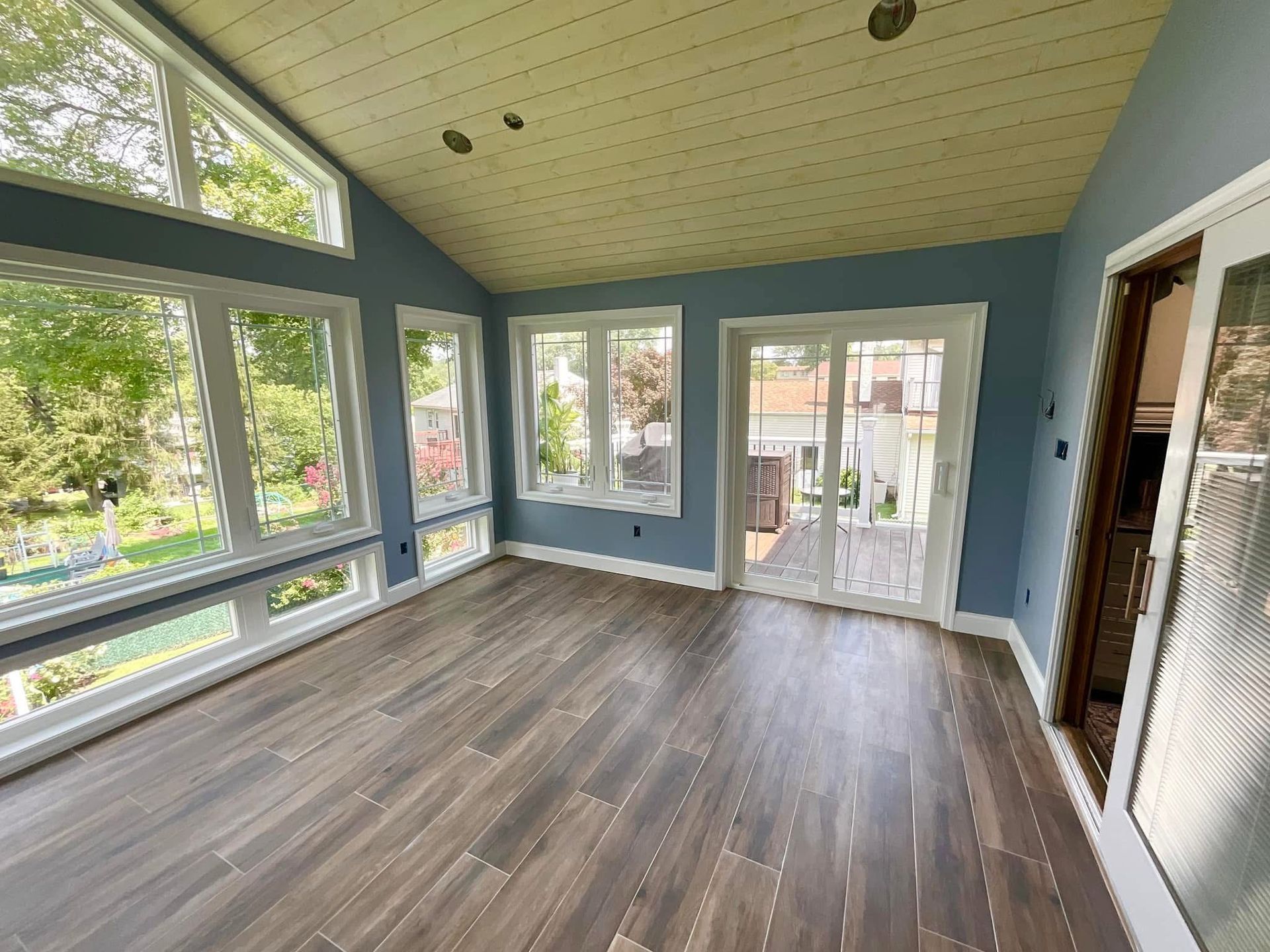 Empty sunroom with large windows, blue walls, wood-look floor, and a glass door to outside