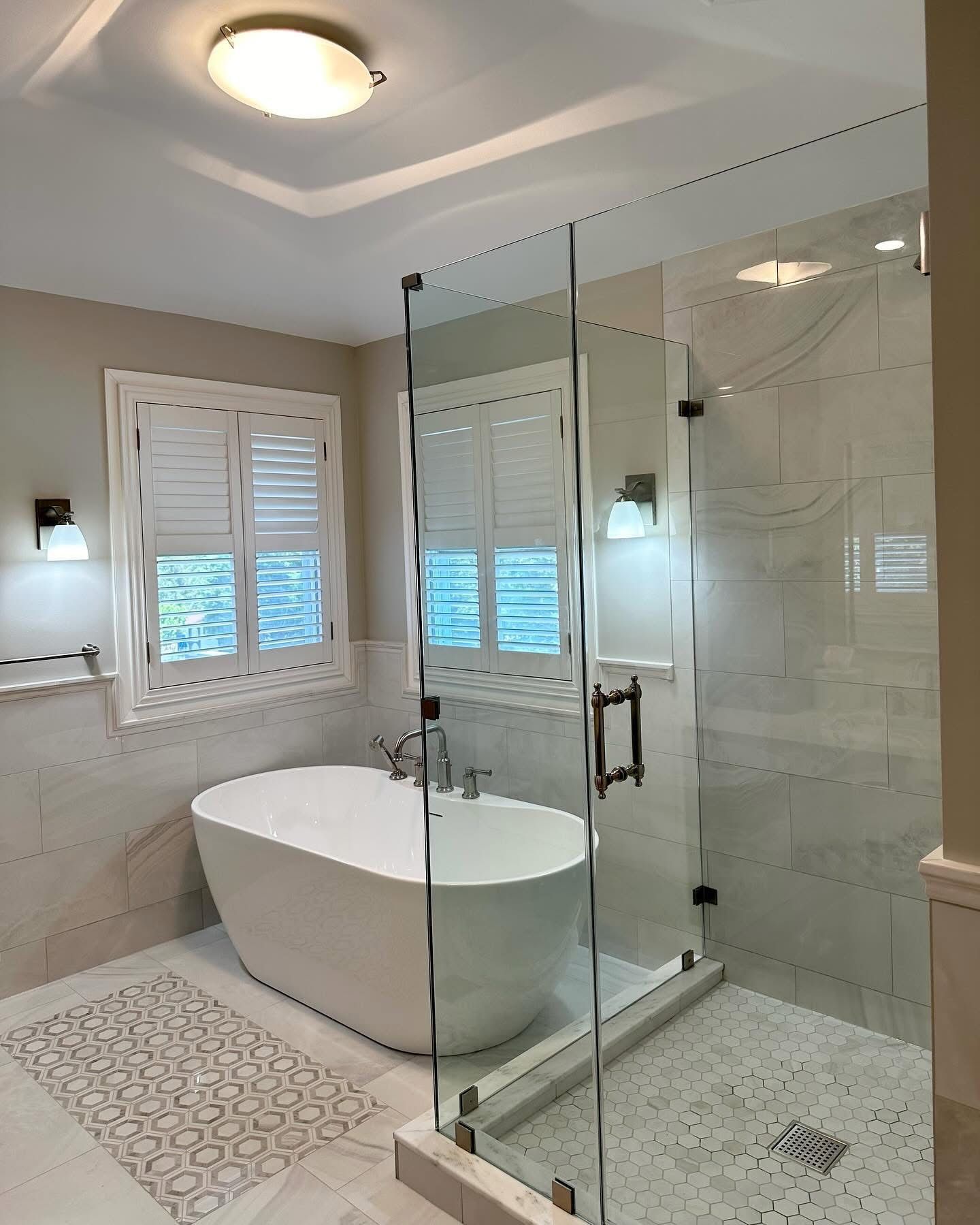 Modern bathroom with freestanding tub, glass shower, marble tile, and window shutters
