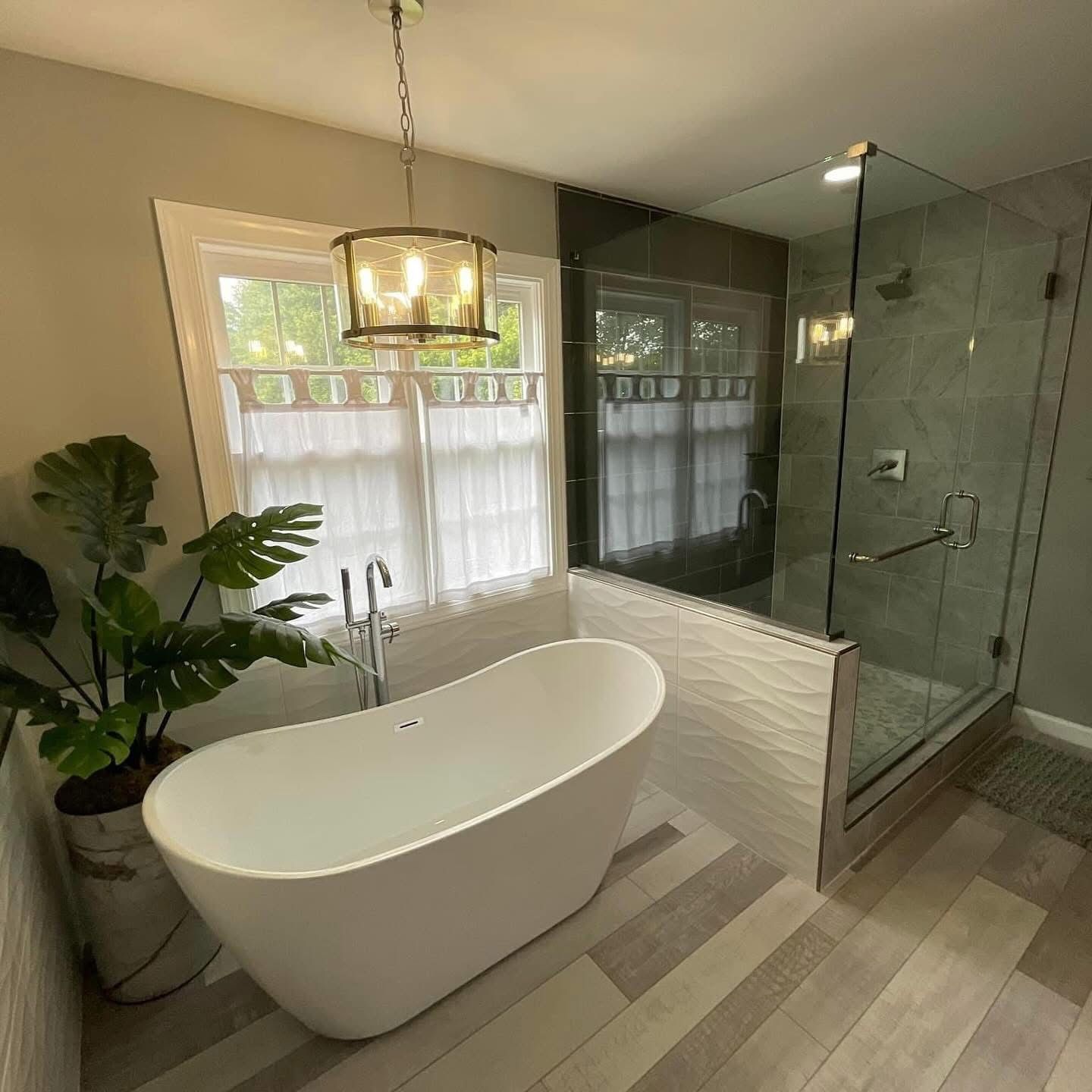 Modern bathroom with freestanding tub, glass shower, and large window with sheer curtains