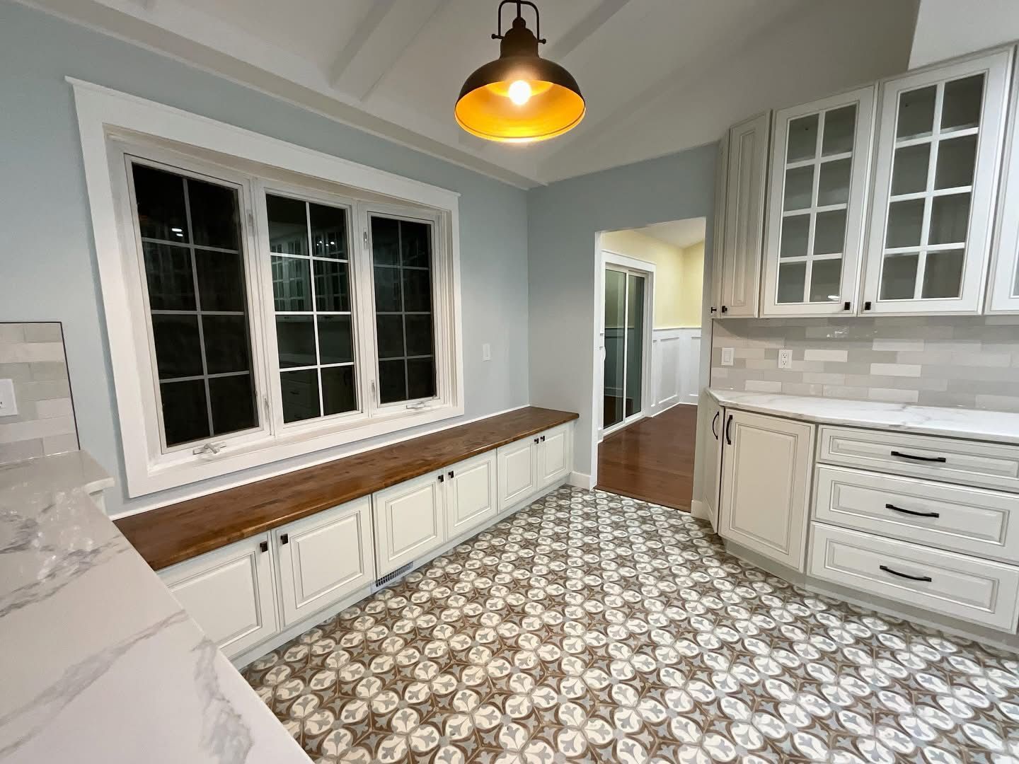 Bright kitchen with white cabinets, patterned tile floor, wood countertop bench, and pendant light