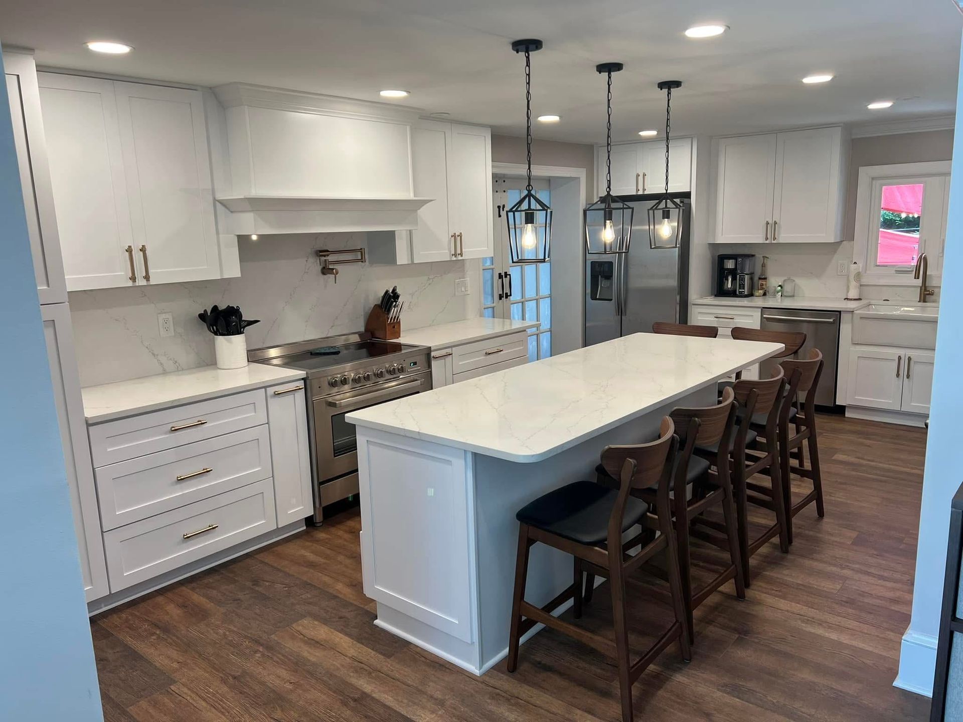 Bright white kitchen with large island, barstools, pendant lights, and hardwood floors