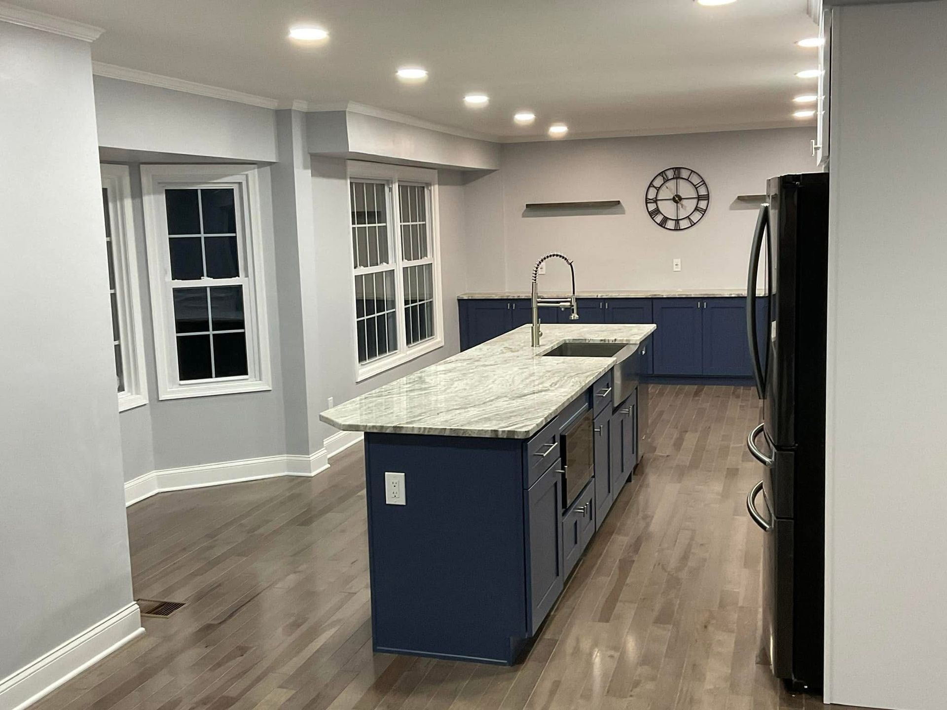 Modern kitchen with blue island, granite counters, white cabinets, and dark wood flooring