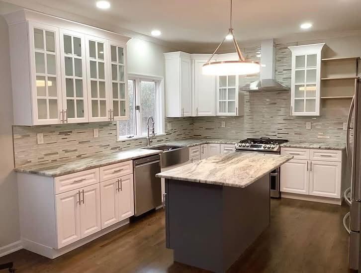 Bright modern kitchen with white cabinets, stone backsplash, island, stainless appliances, and wood floors