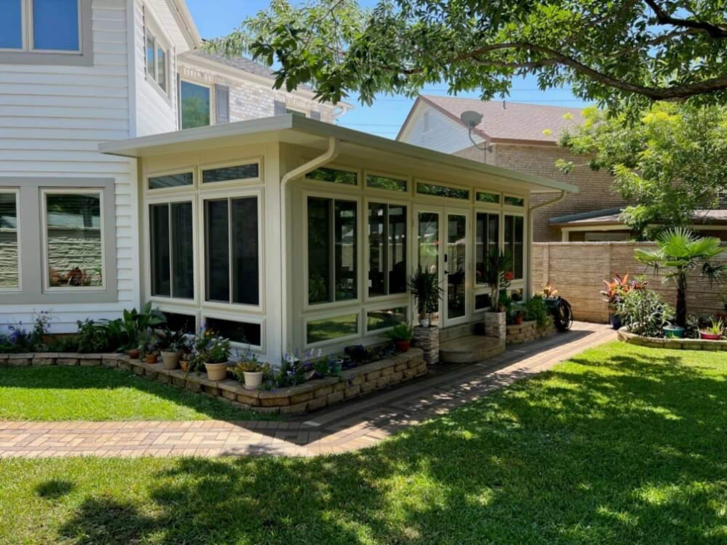 House side porch with white trim, large windows, and a stone planter in a sunny yard