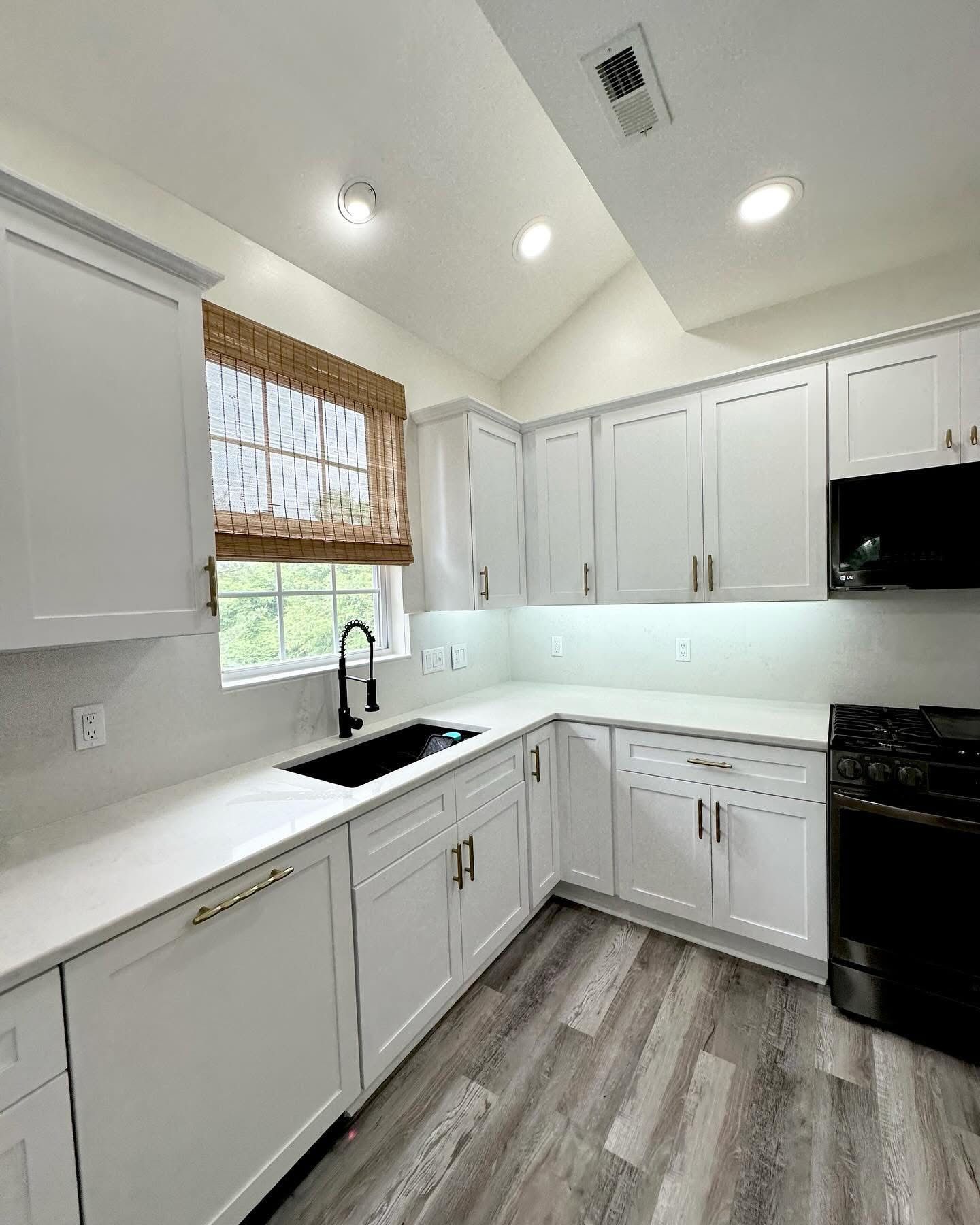 Bright white kitchen with black appliances, white cabinets, and a window above the sink