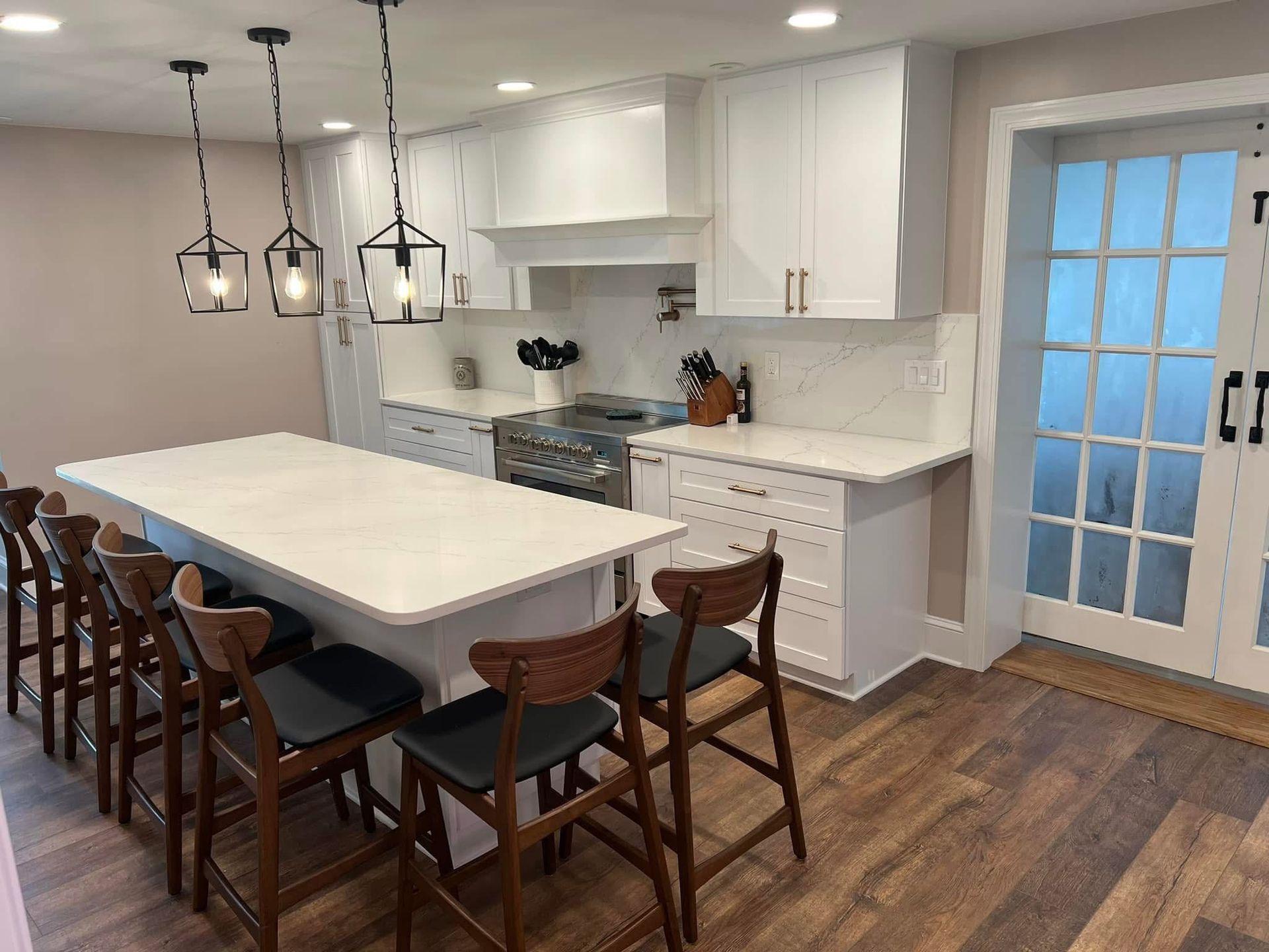 Modern kitchen with white cabinets, island, pendant lights, wood floors, and a dining table with chairs
