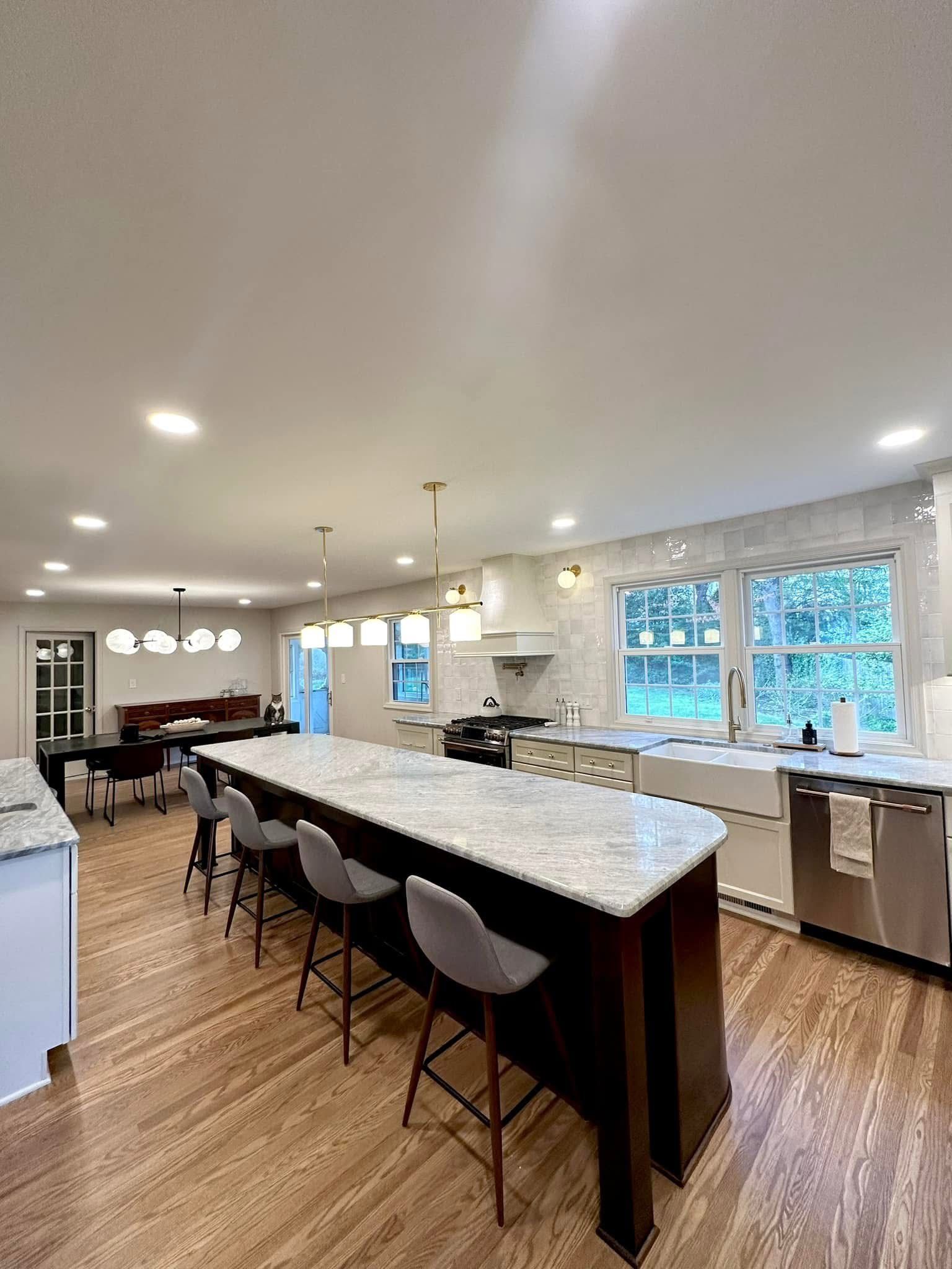 Bright modern kitchen with white cabinets, large island, bar stools, and large windows.