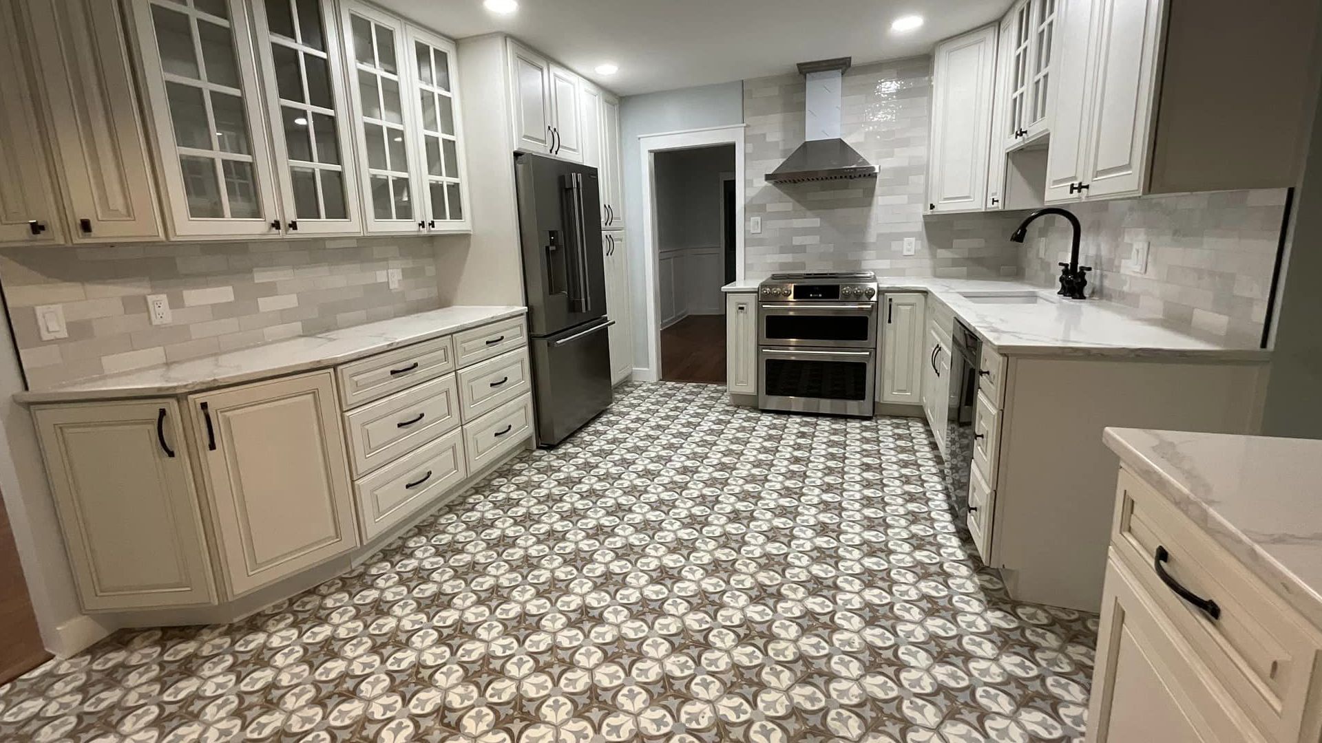 Bright kitchen with white cabinets, patterned tile floor, stainless steel appliances, and an island sink.