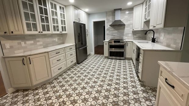 Bright kitchen with white cabinets, patterned tile floor, stainless steel appliances, and an island sink.