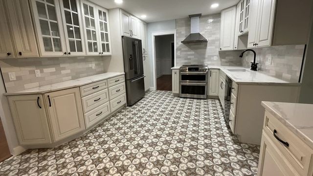 Bright kitchen with white cabinets, patterned tile floor, stainless steel appliances, and an island sink.