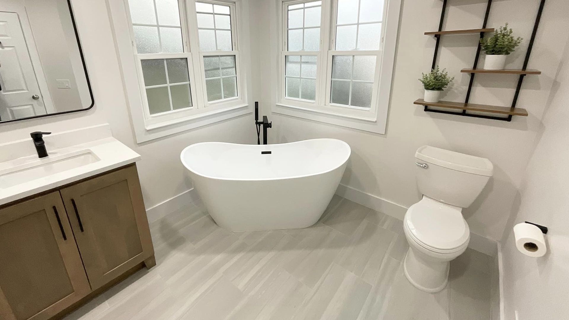 Bright modern bathroom with a freestanding tub, vanity, toilet, and window shelves