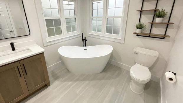 Bright modern bathroom with a freestanding tub, vanity, toilet, and window shelves