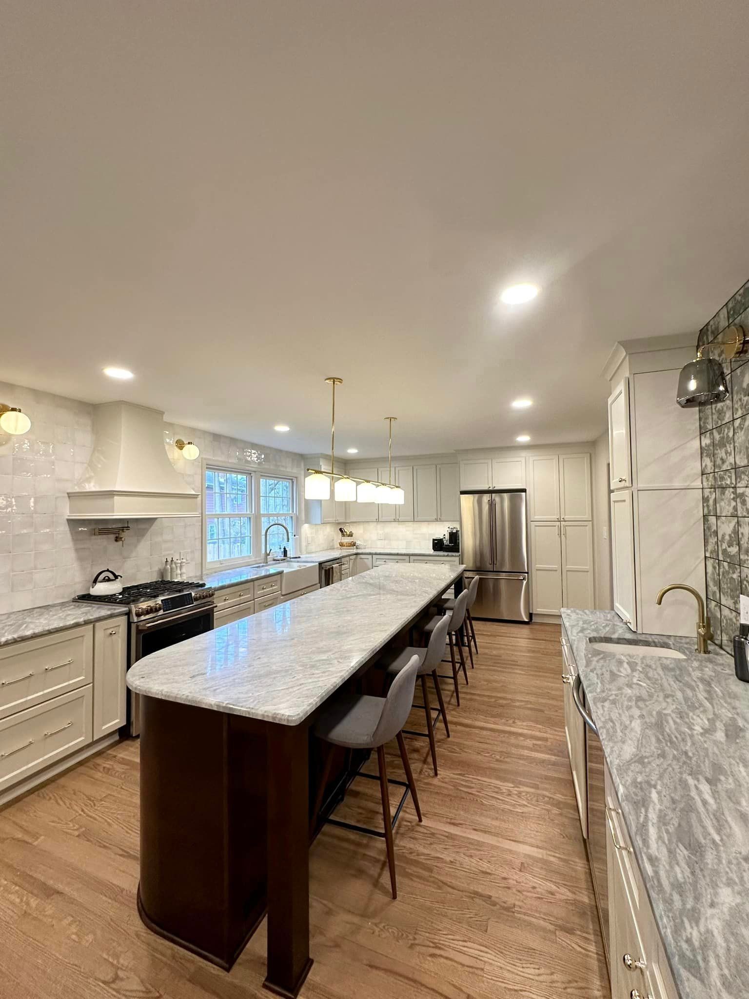Bright modern kitchen with a long island, bar stools, white cabinets, and hardwood floors.