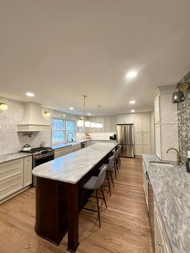Bright modern kitchen with a long island, bar stools, white cabinets, and hardwood floors.