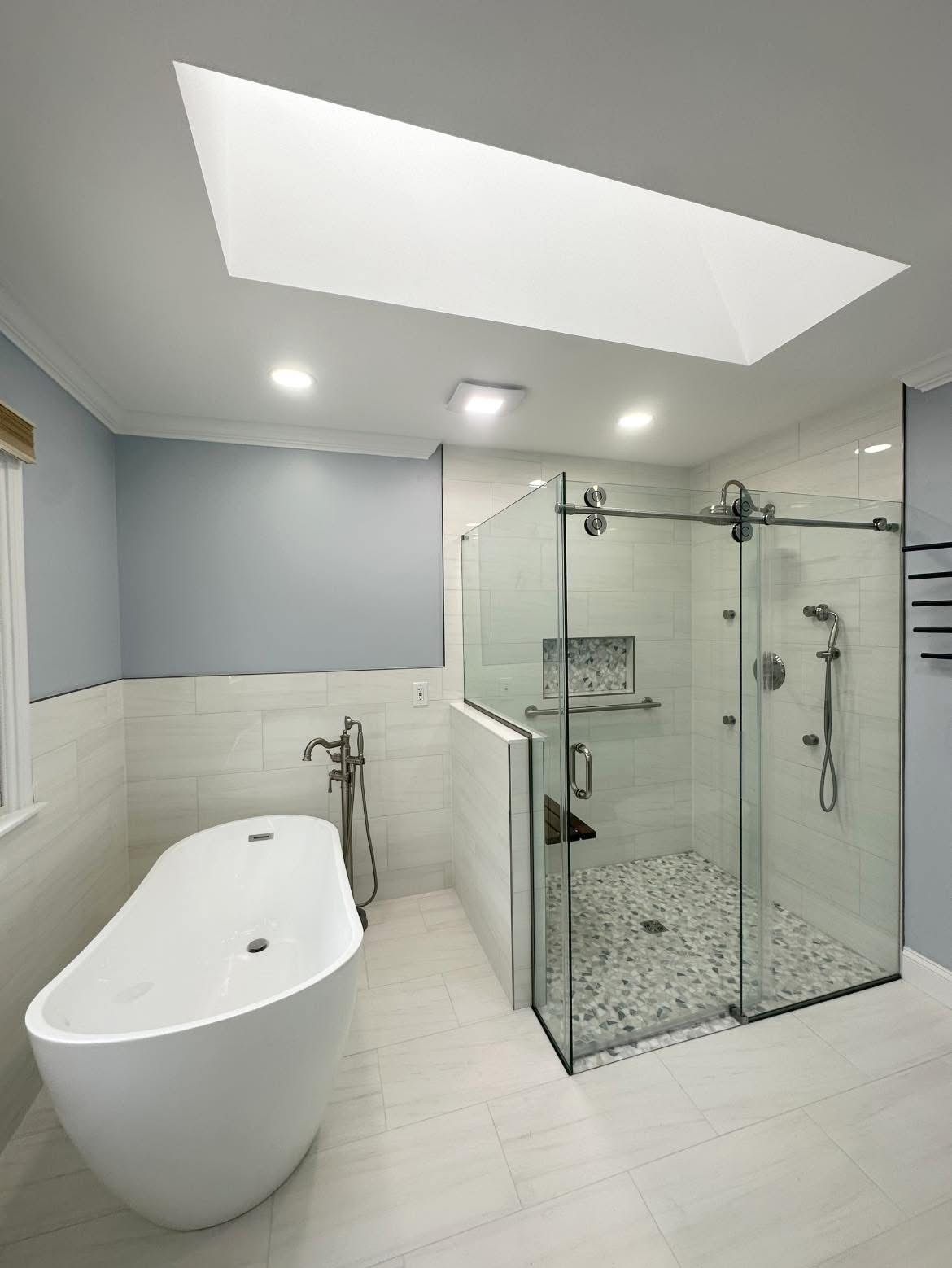 Modern white bathroom with freestanding tub, glass shower, and skylight