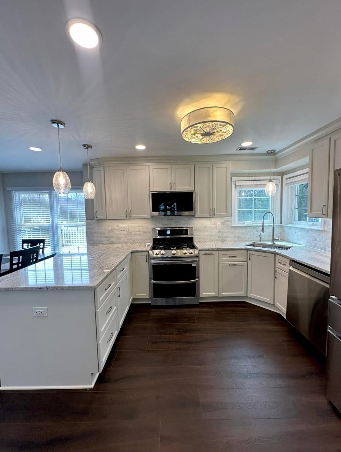 Modern white kitchen with dark wood floors, island, stainless steel appliances, and pendant lighting
