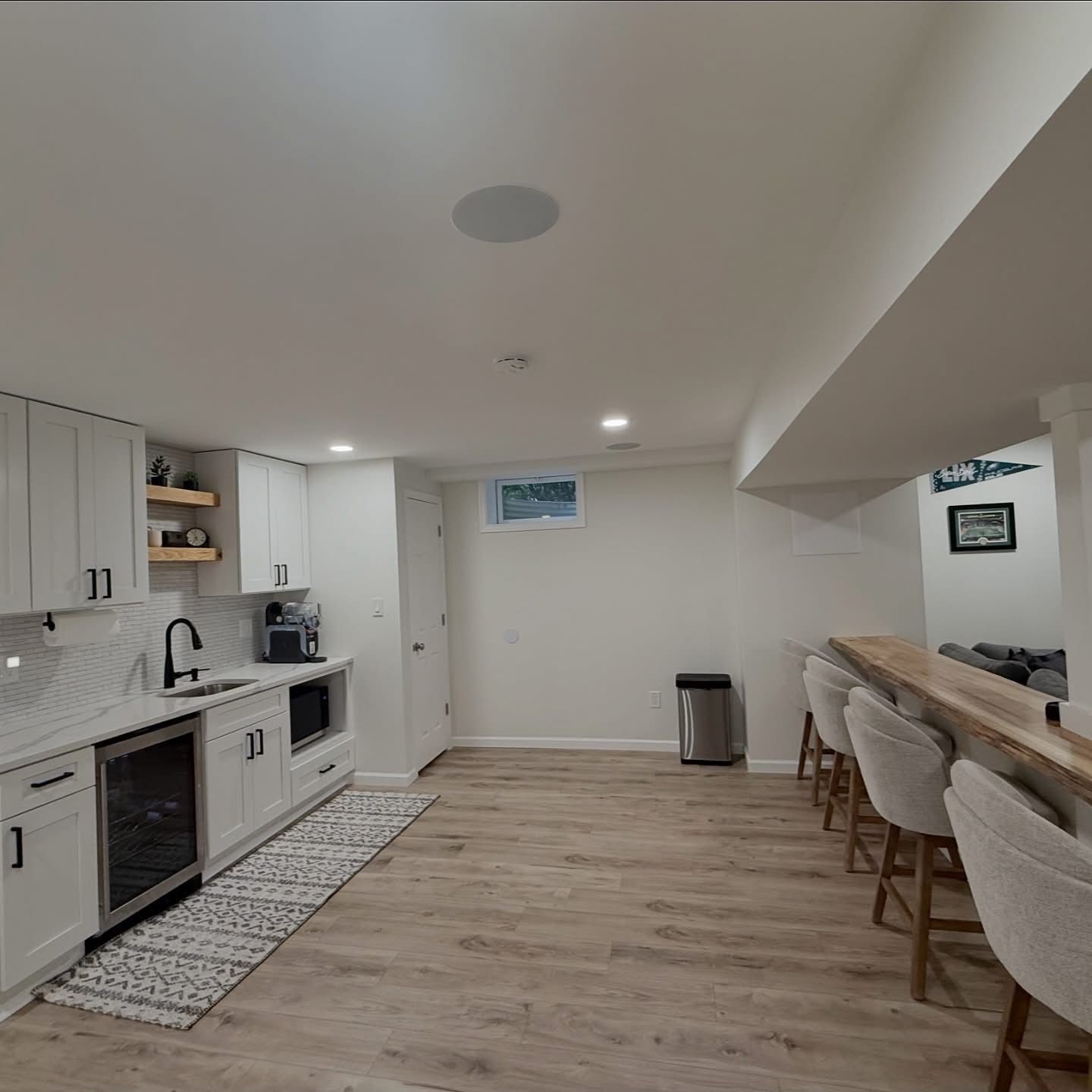 Modern basement kitchen and bar area with white cabinets, light wood floors, and stools along a counter.