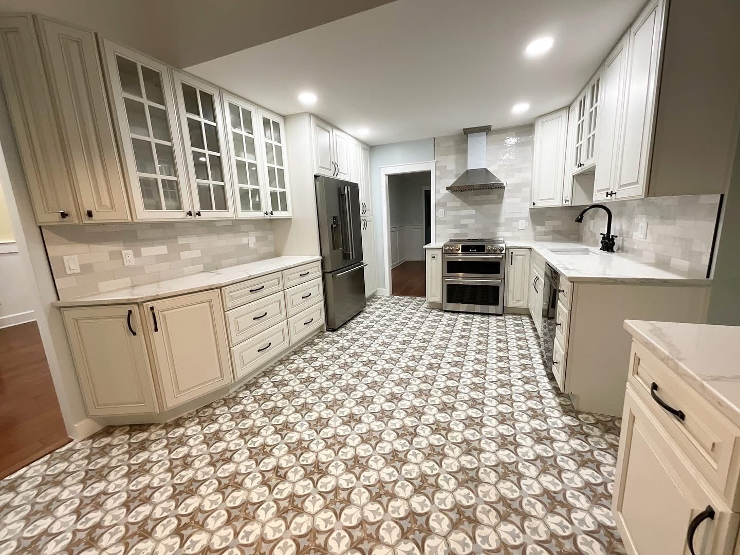 Bright kitchen with white cabinets, patterned tile floor, stainless fridge, and granite countertops.